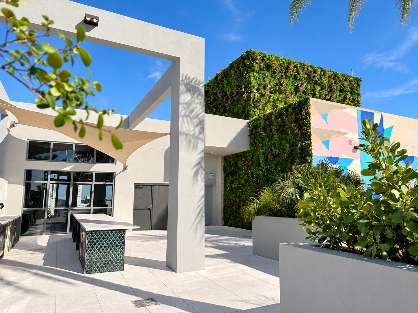 Rooftop amenity deck with a multi-level greenwall wrapping the building core, framed by a pergola, shade sail, outdoor kitchen and mural