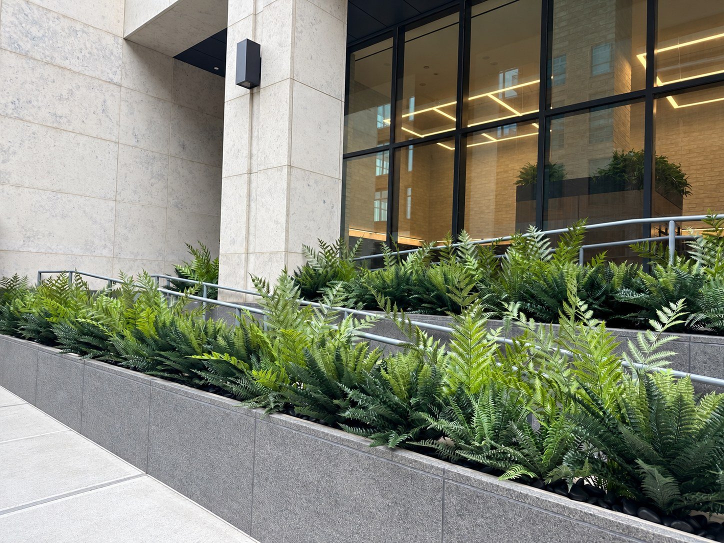 Granite planters filled with layered artificial ferns along a residential building entry ramp in Brooklyn, NY