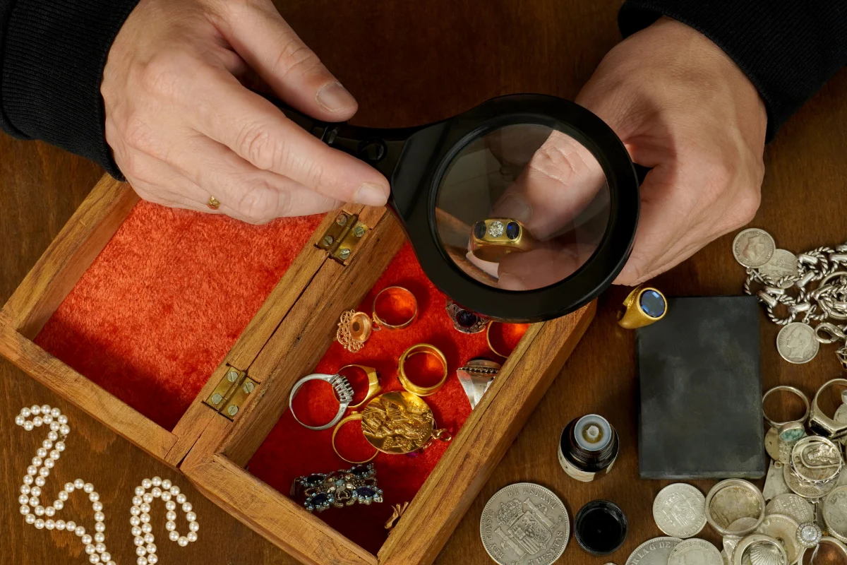 Jewelry being examined with a magnifying glass alongside rings, silver and coins