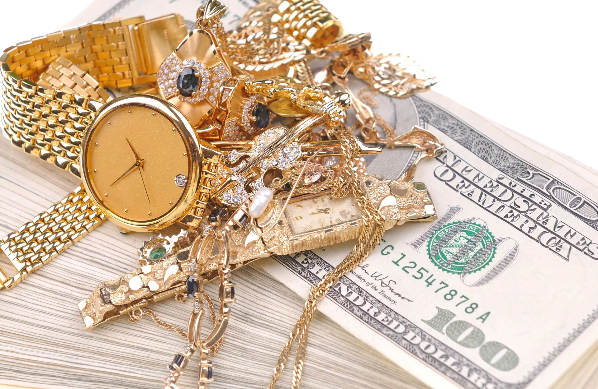 Gold jewelry and watches resting on U.S. currency