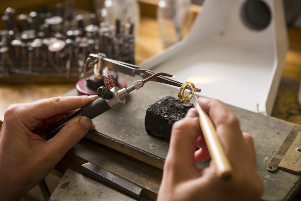 Jeweler using a torch to repair a gold ring at the workbench