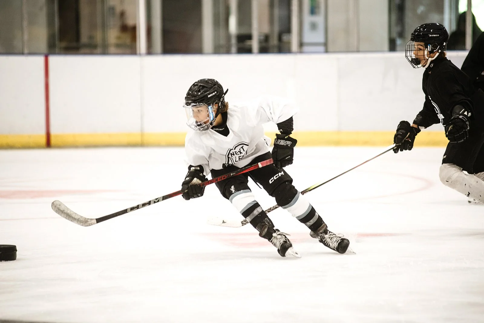 Young skater in a Next Level jersey driving to the puck