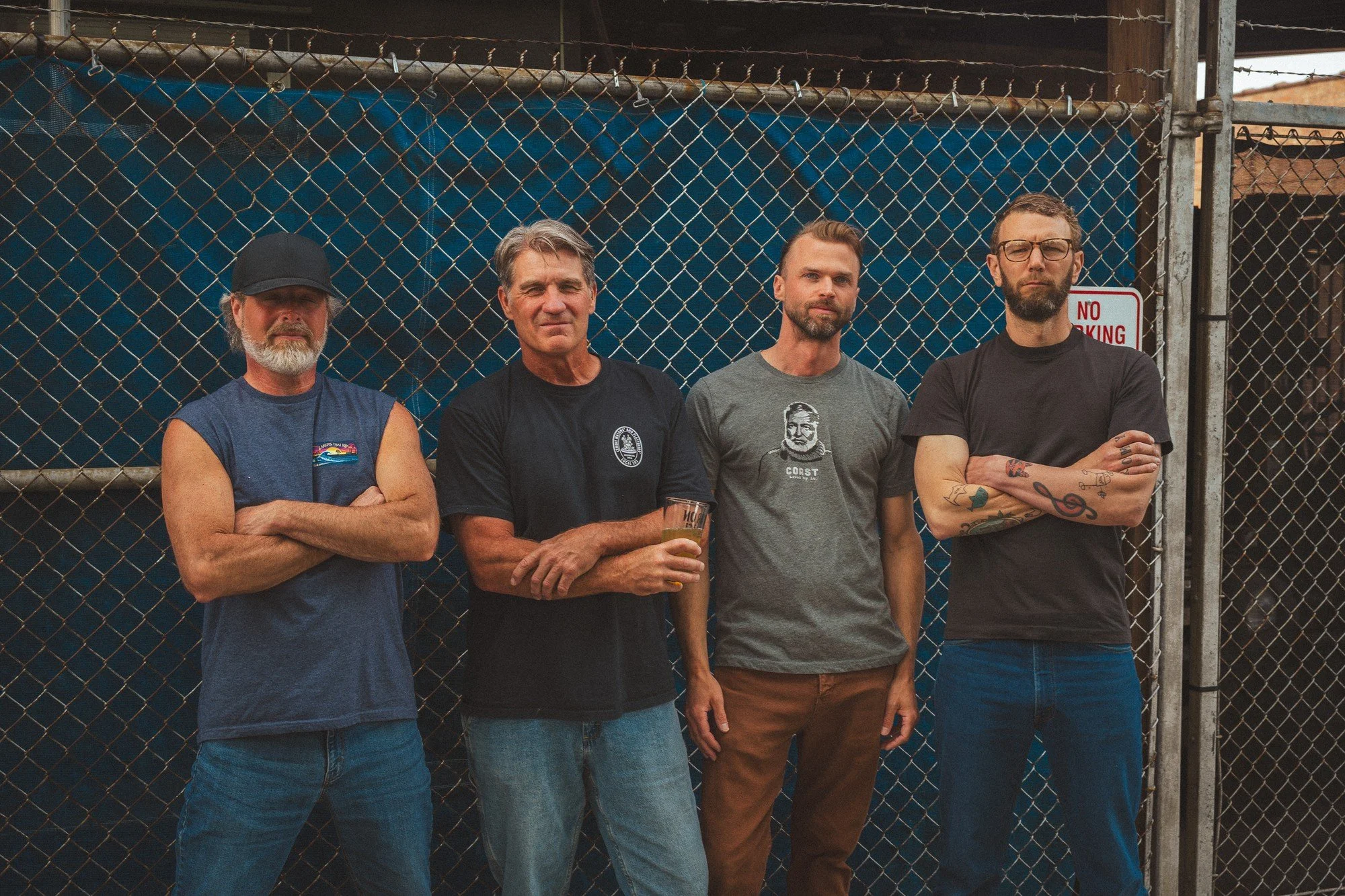 Four band members stand in front of a blue fence for a group portrait.