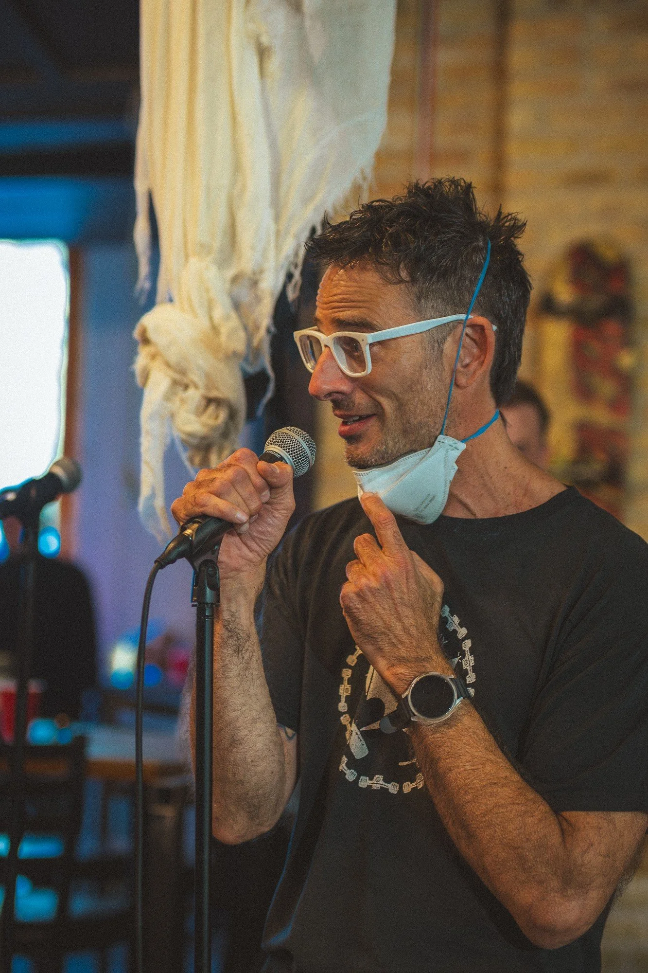 A performer wearing light-colored glasses holds a microphone close to their face.