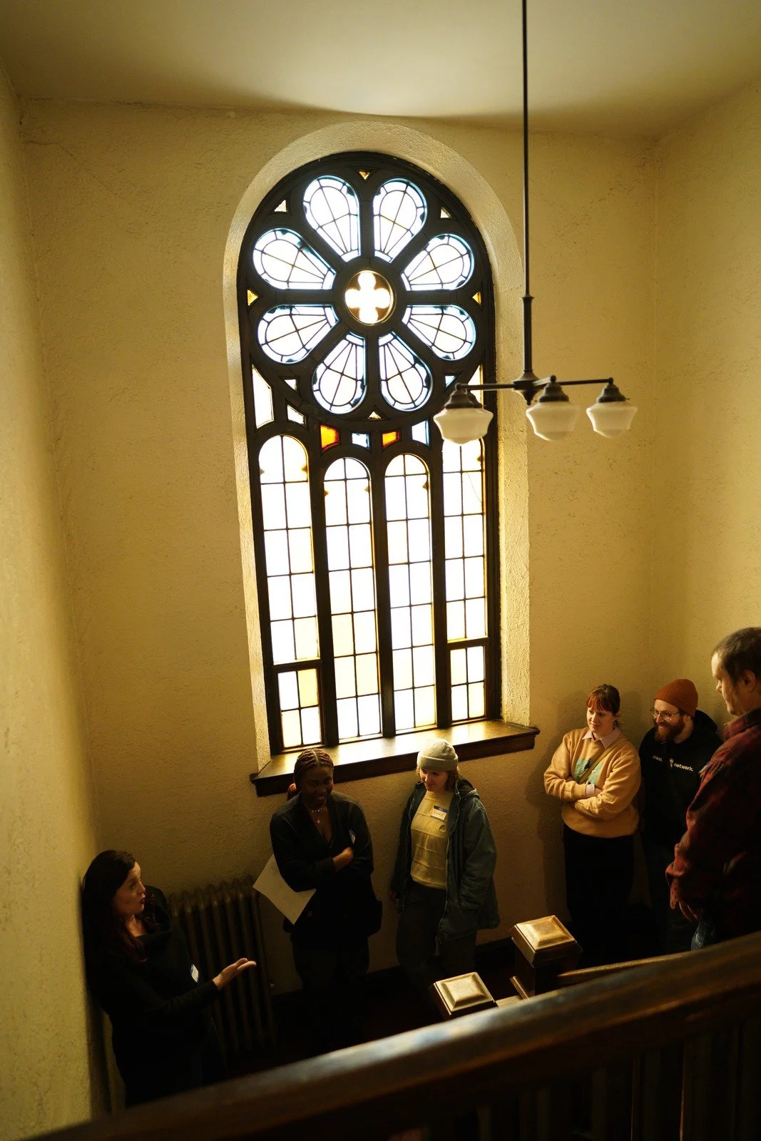 Visitors gather beneath a tall stained-glass window.