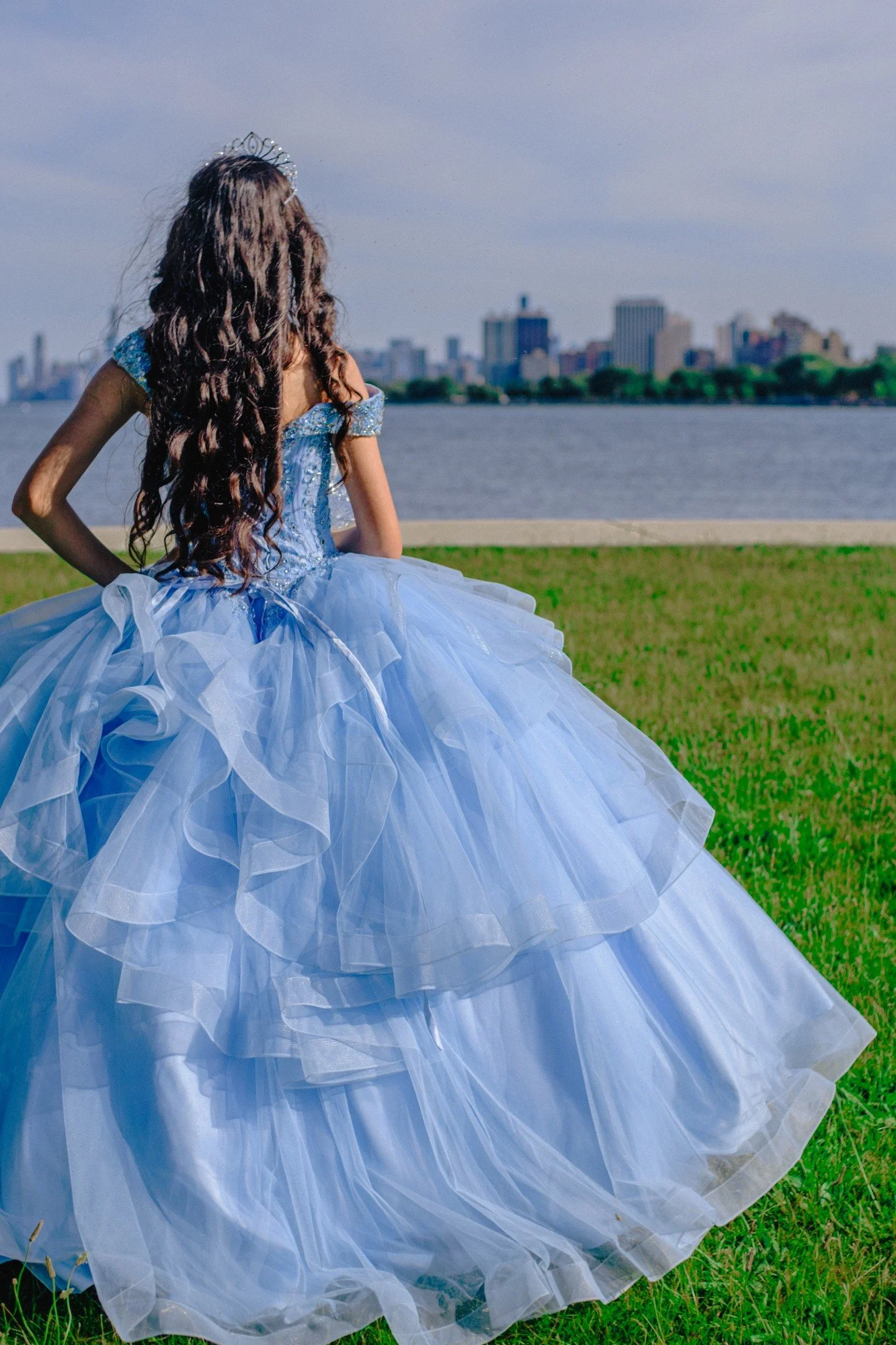 A blue layered gown moves across the grass in a portrait photographed from behind.