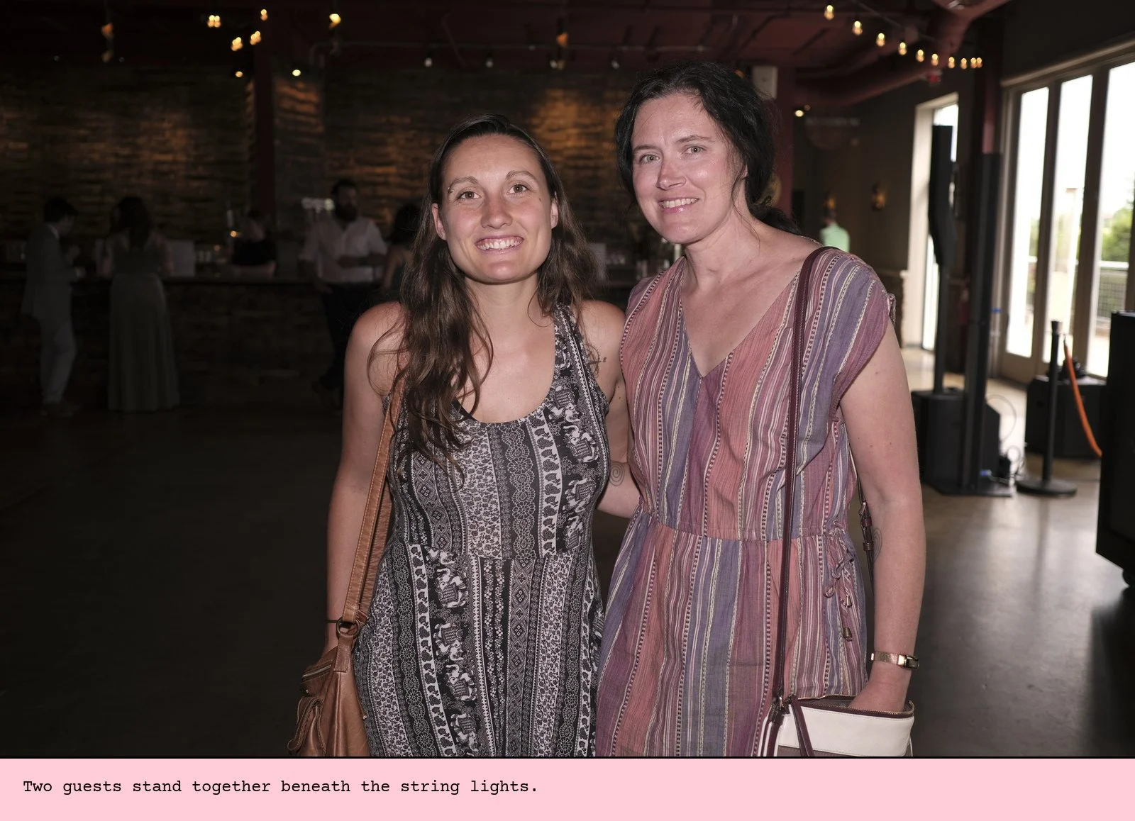 Two guests stand together beneath the string lights.