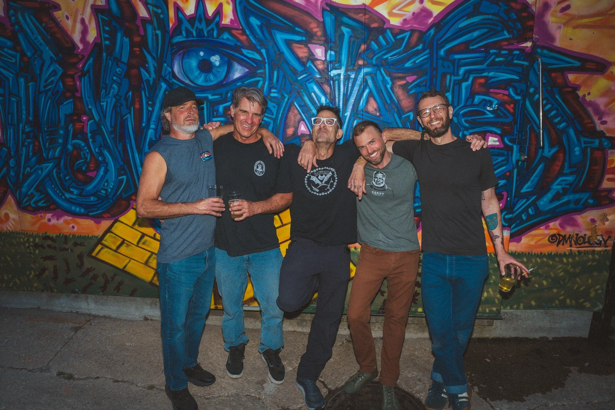 Five people pose together against a brightly painted mural.