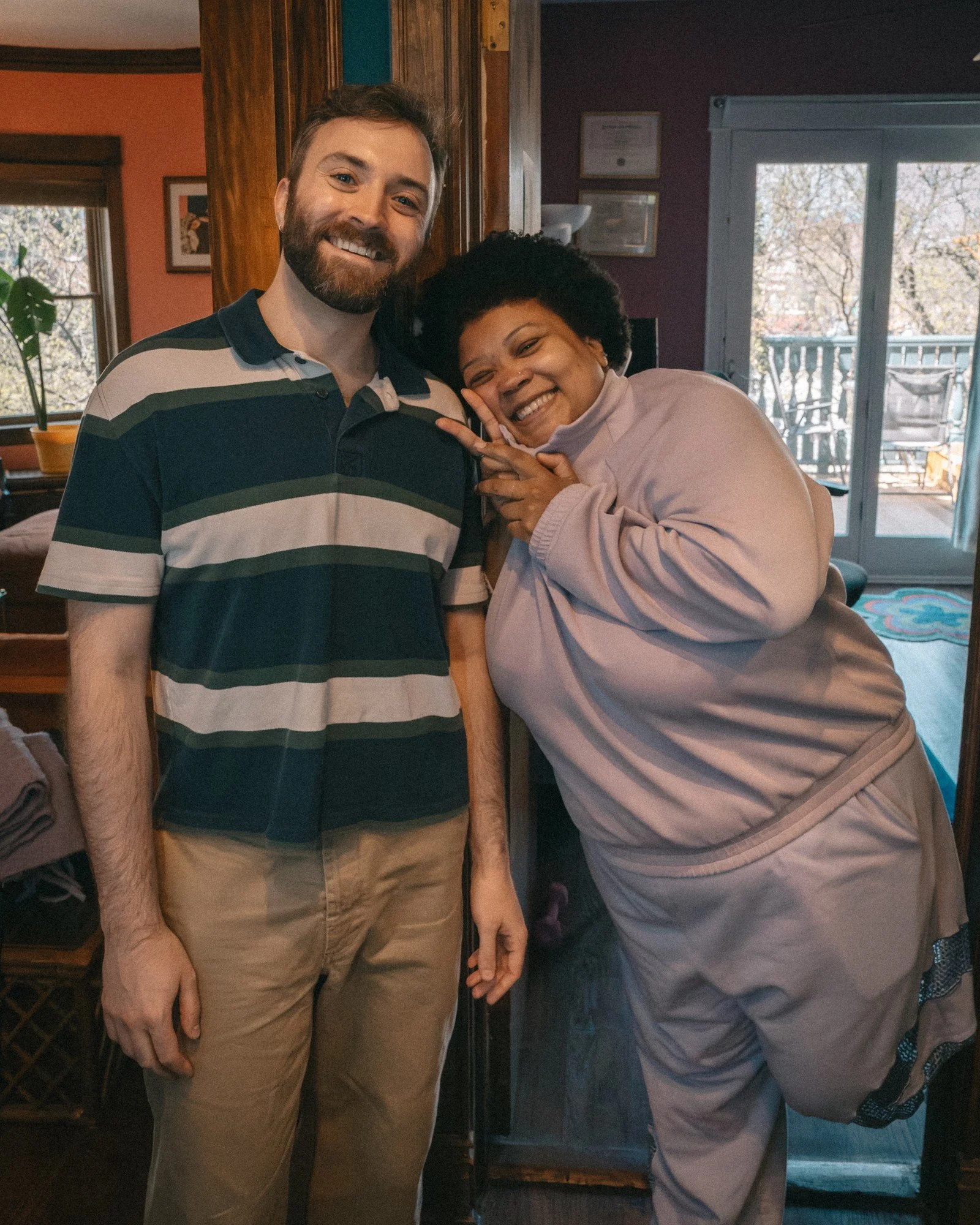 Two people lean together and smile in a room filled with framed art.
