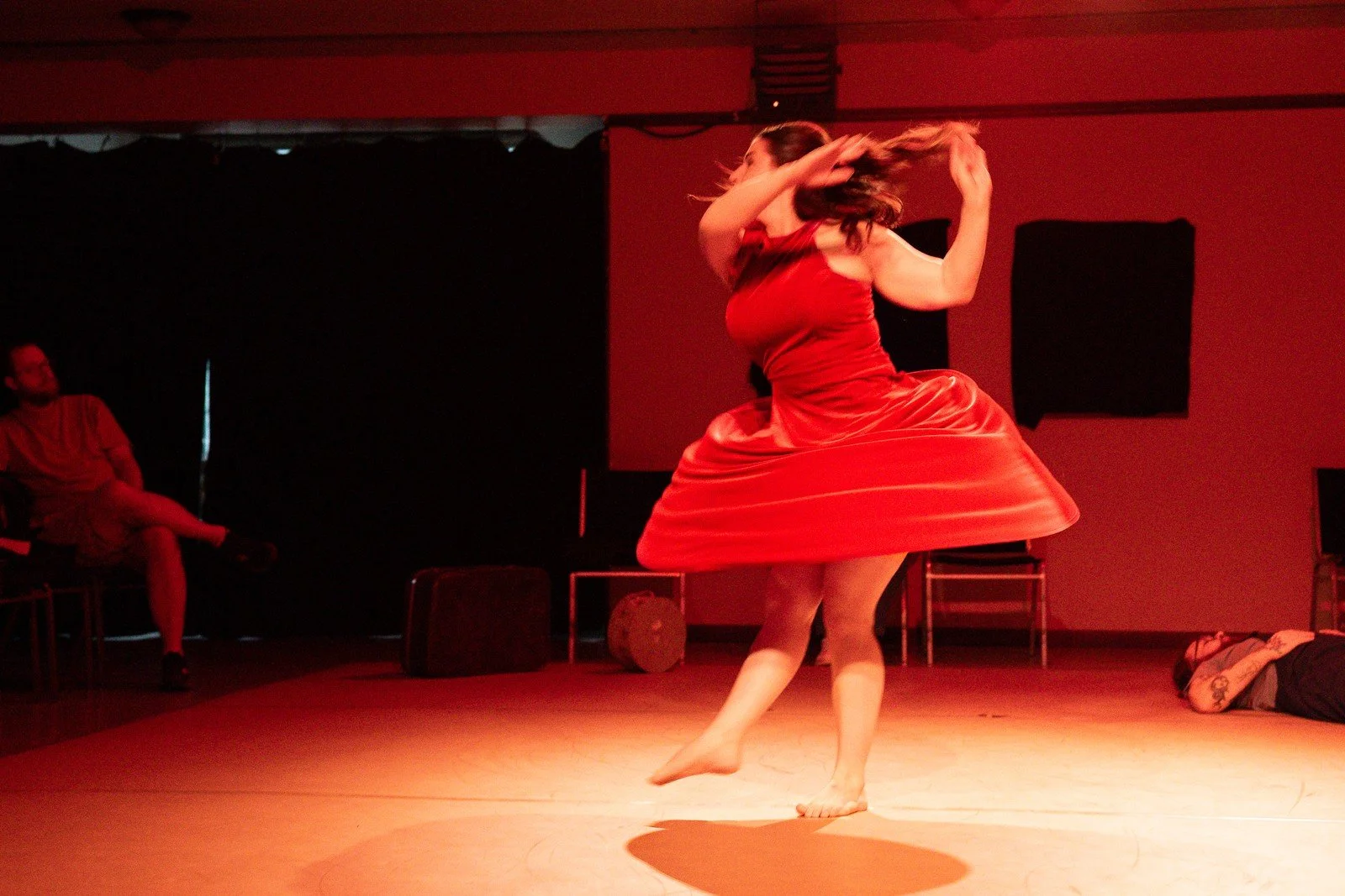 A dancer in a red dress turns beneath warm stage lighting.