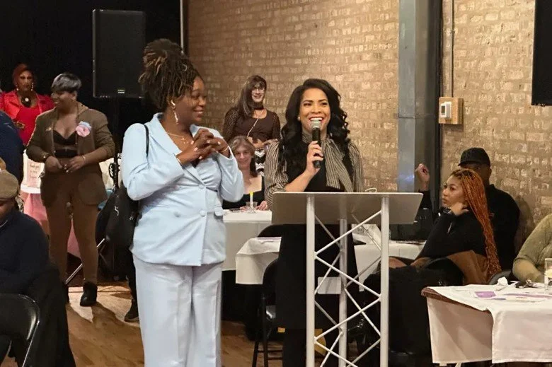 Zahara Bassett stands beside Precious Brady-Davis as she speaks into a microphone at a lectern.