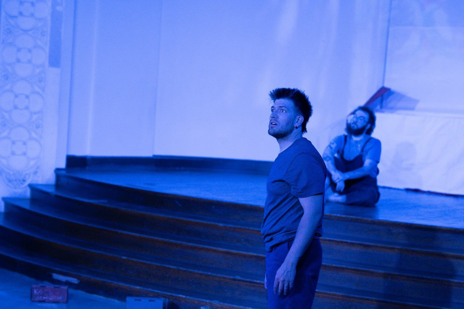 Two performers pause beside a stage under blue lighting.