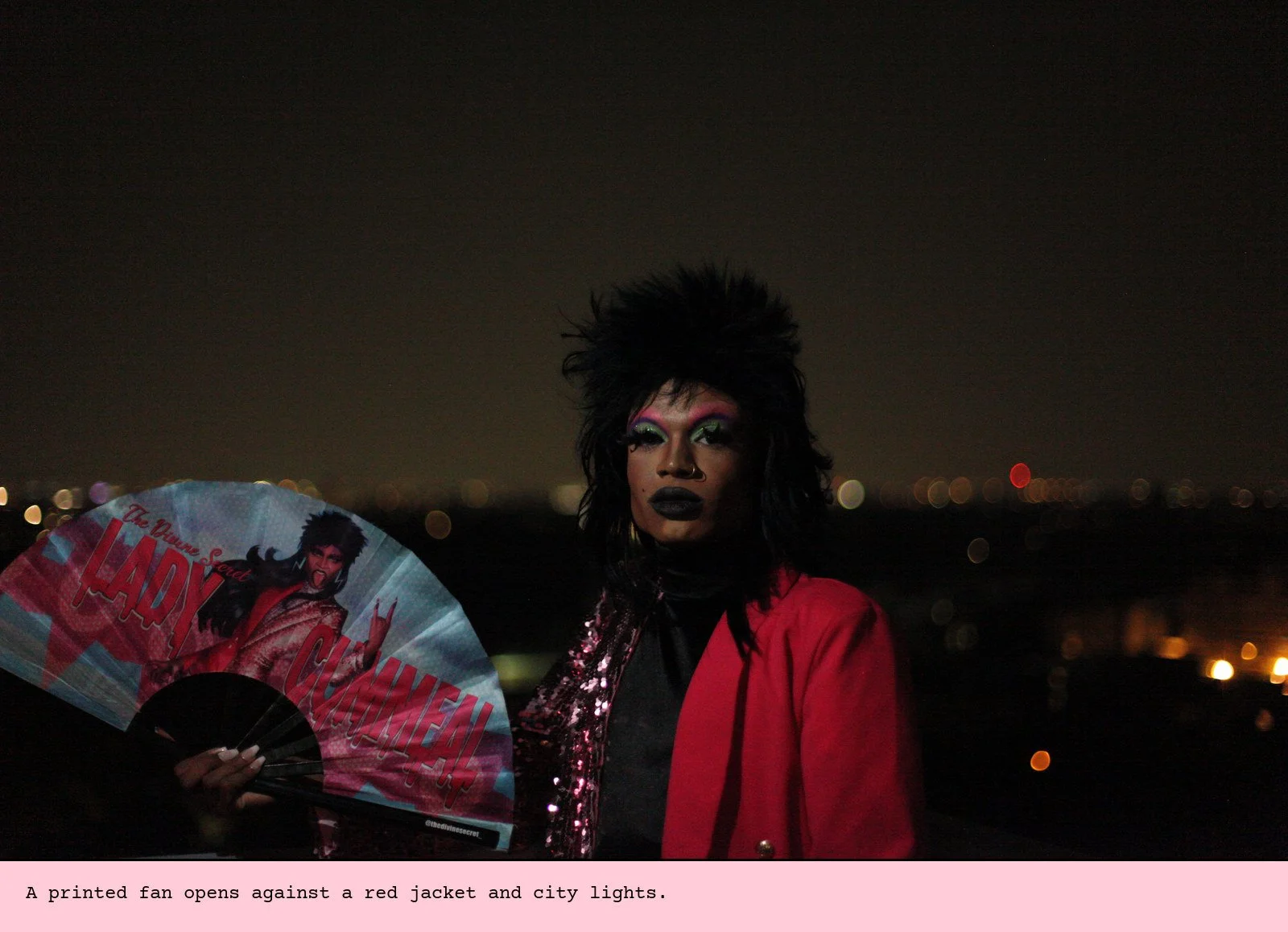 A printed fan opens against a red jacket and city lights.