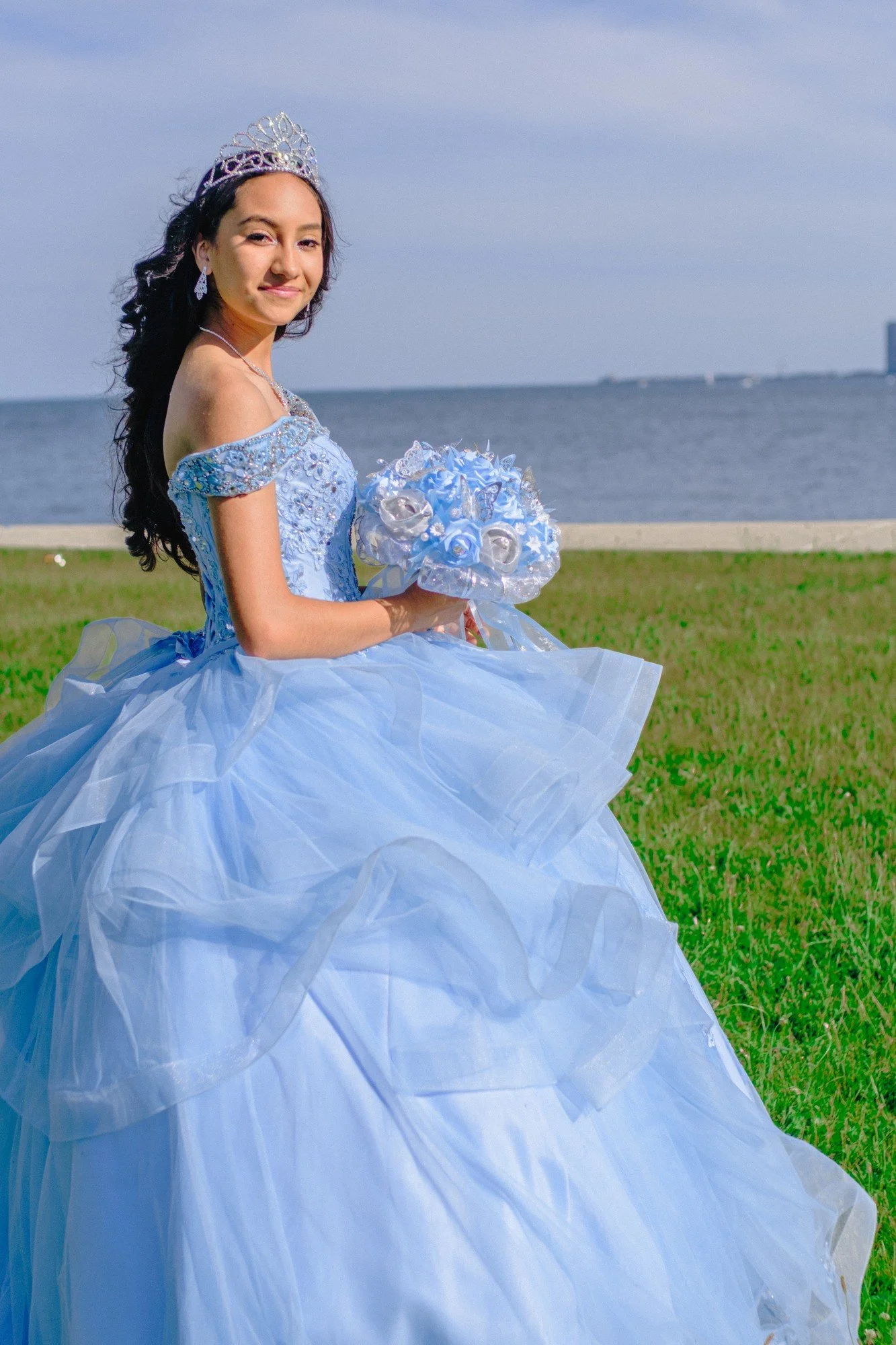 A person in a blue gown turns toward the camera while holding a bouquet.