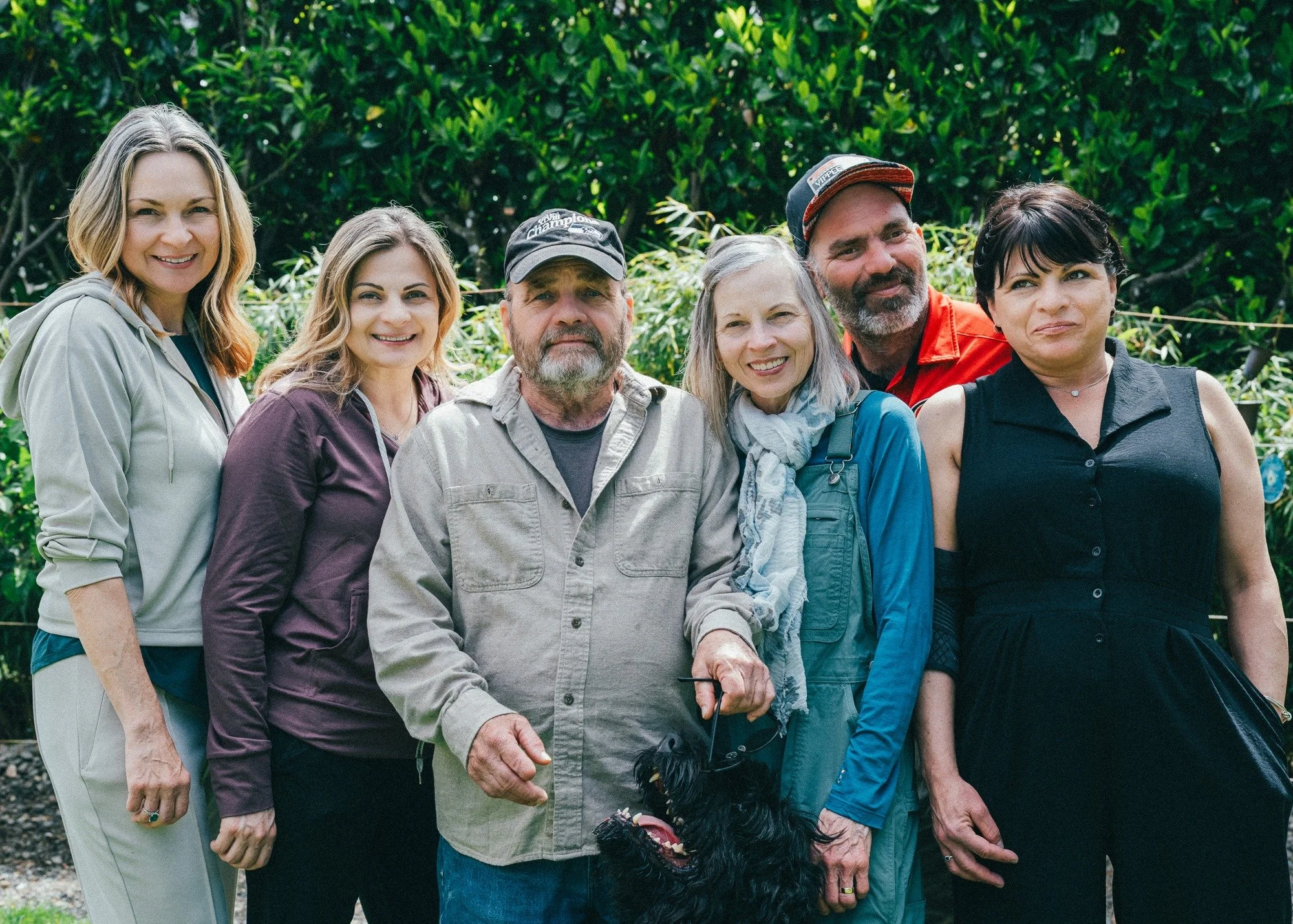 Six people stand shoulder to shoulder in a garden.