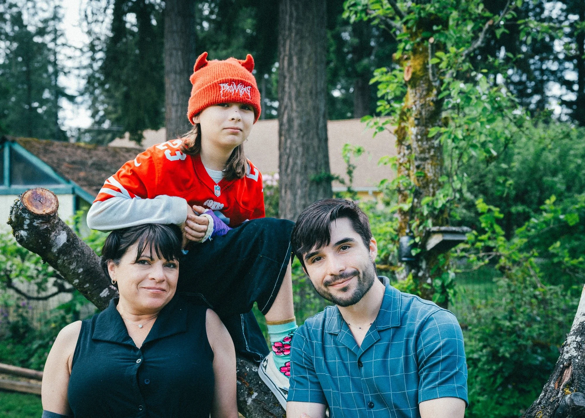 Three people gather around a low tree branch for a portrait.