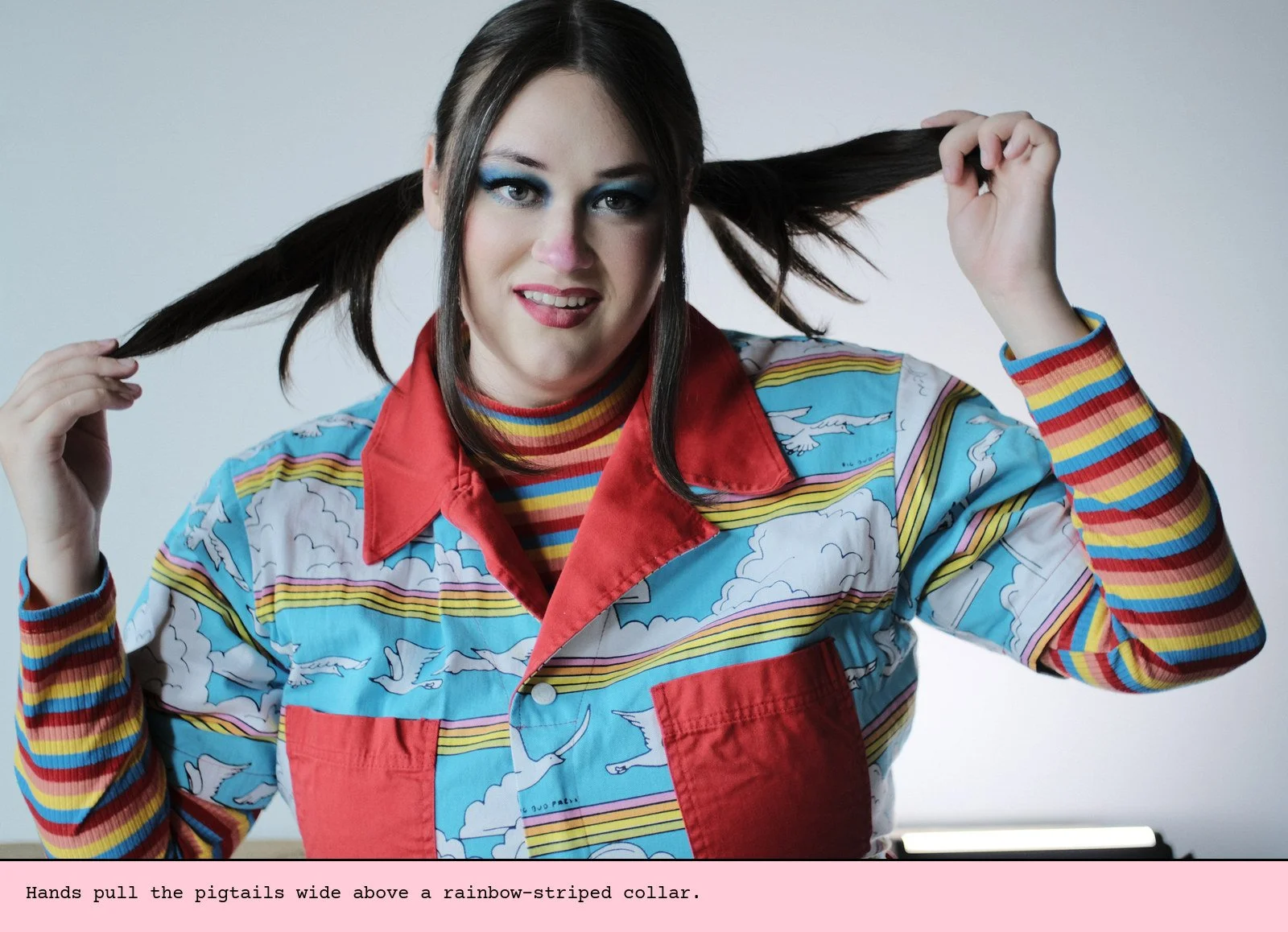 Hands pull the pigtails wide above a rainbow-striped collar.