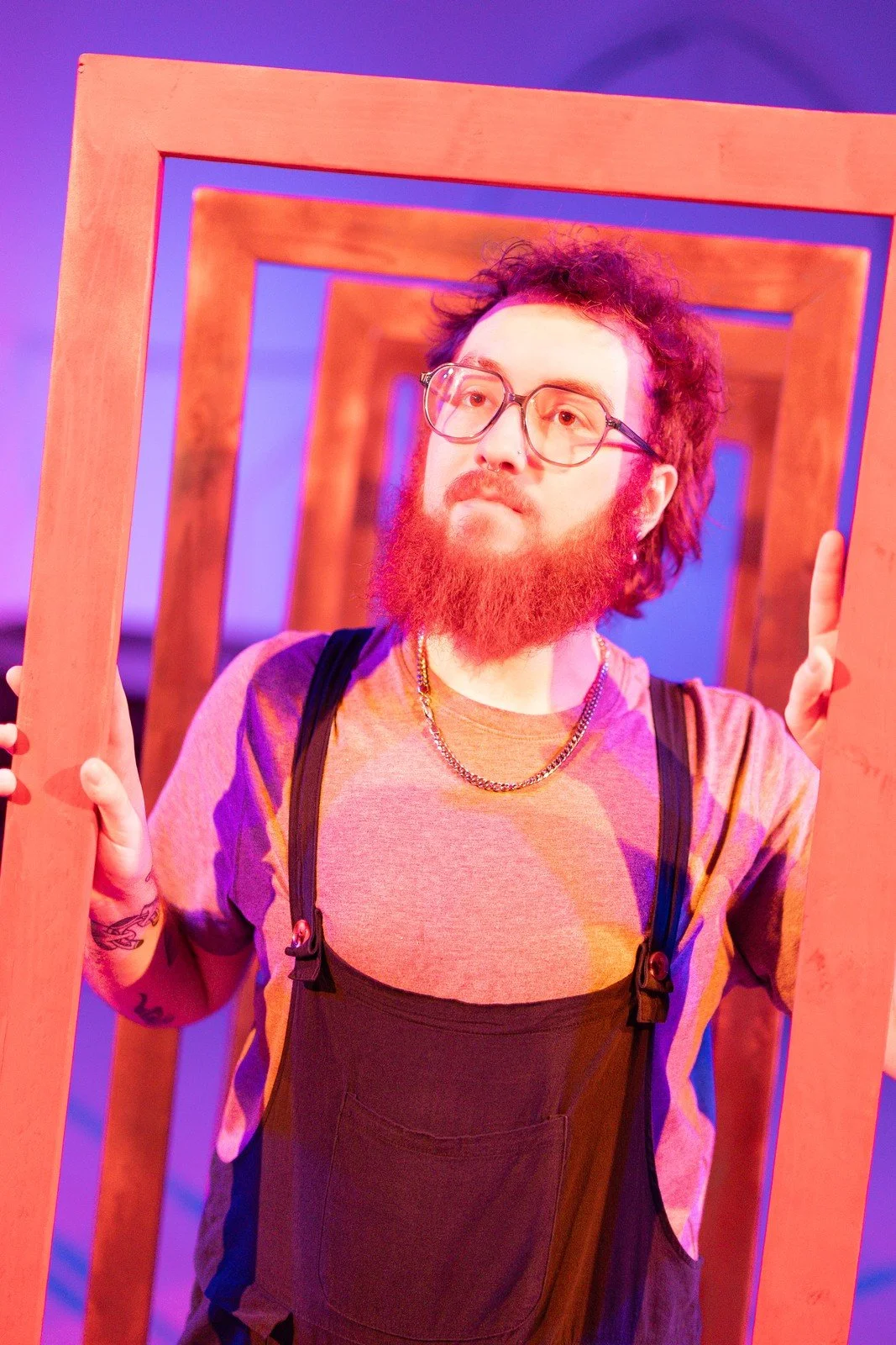 A performer poses within a series of wooden frames lit in pink and purple.