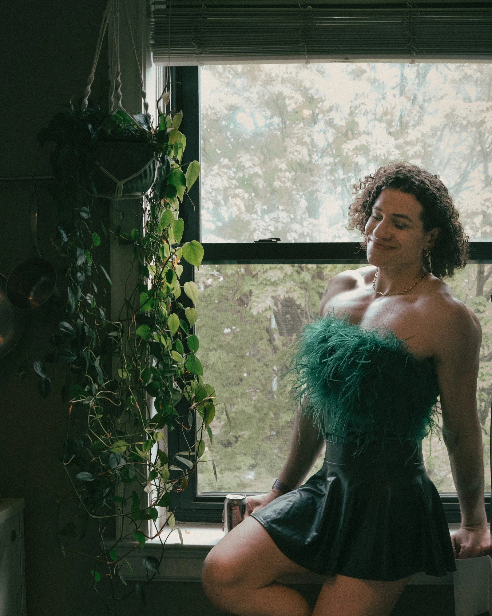 A person in a green dress sits beside a window framed by houseplants.