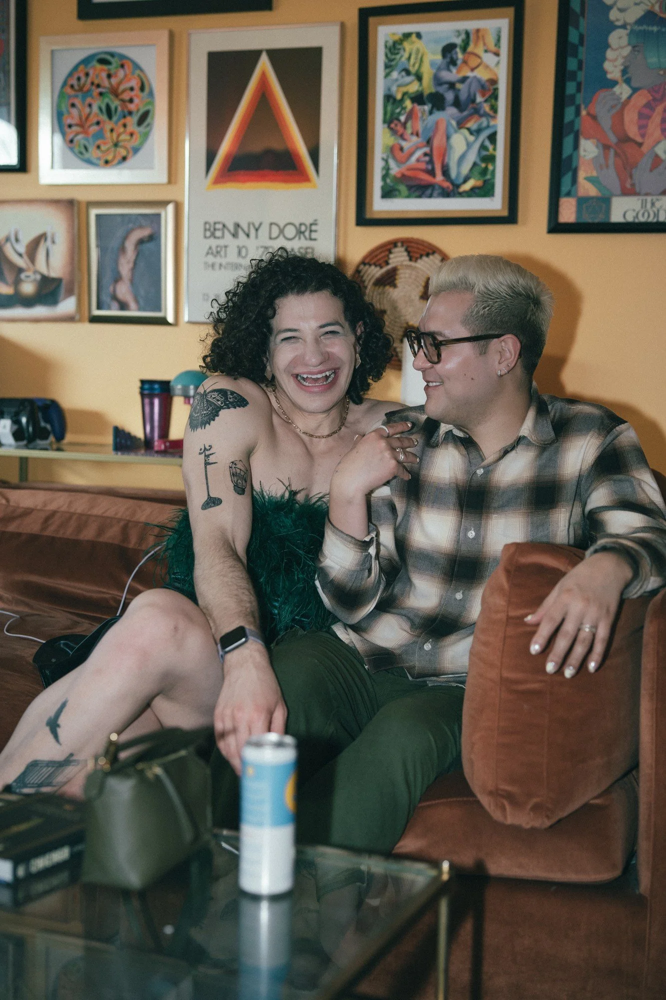 Two guests sit together and laugh on a sofa surrounded by framed artwork.