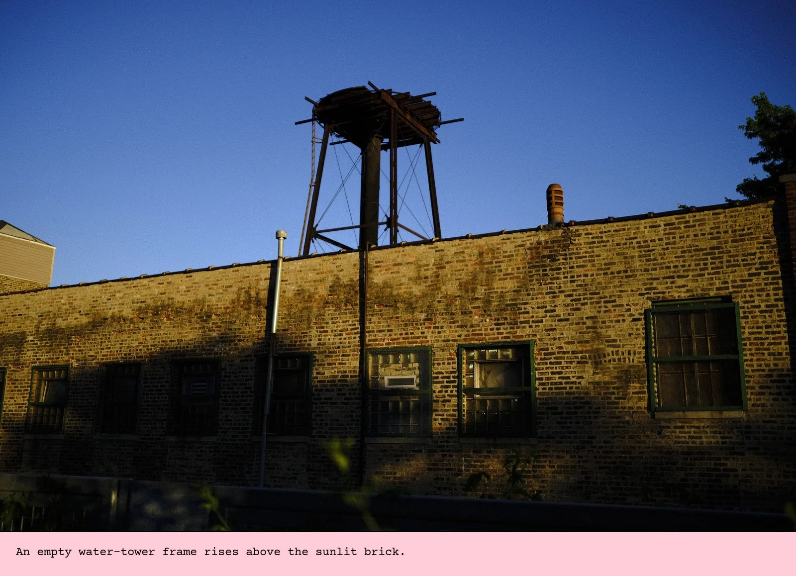 An empty water-tower frame rises above the sunlit brick.