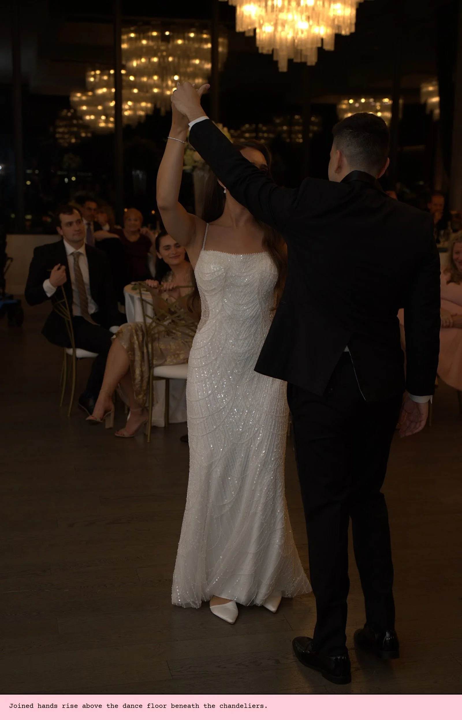 Joined hands rise above the dance floor beneath the chandeliers.