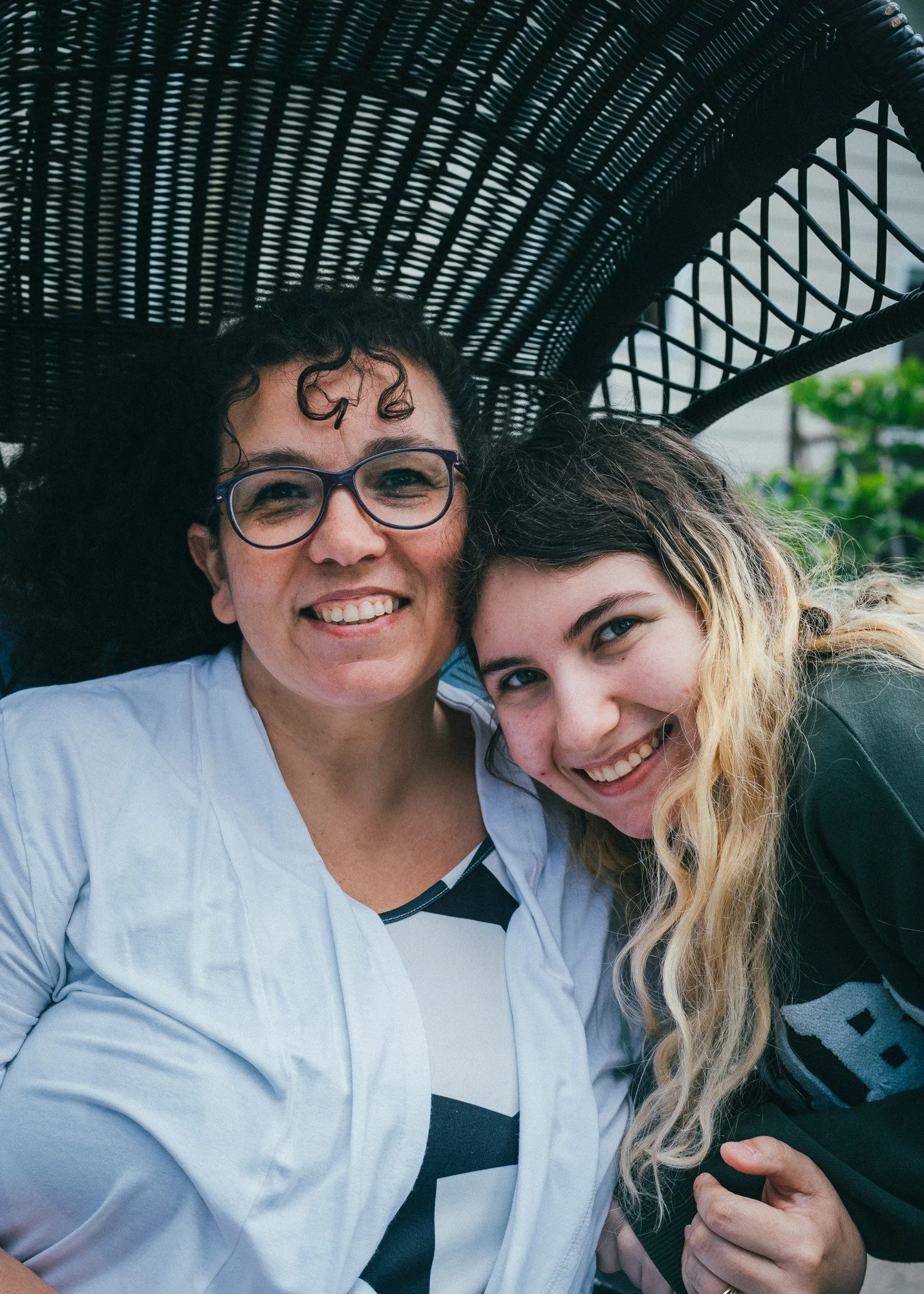 Two people smile beneath a dark woven garden chair canopy.