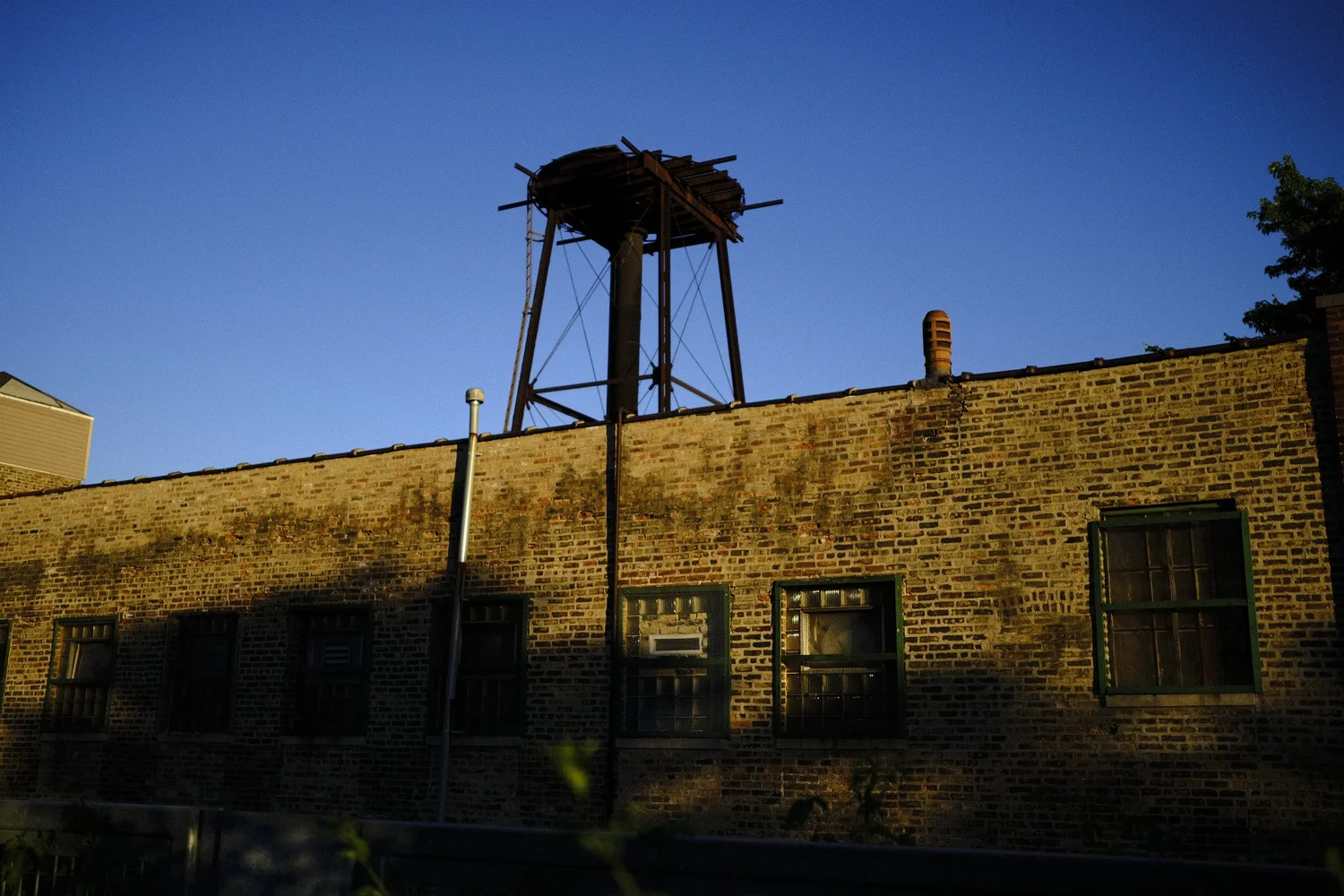 An empty water-tower frame rises above the sunlit brick.