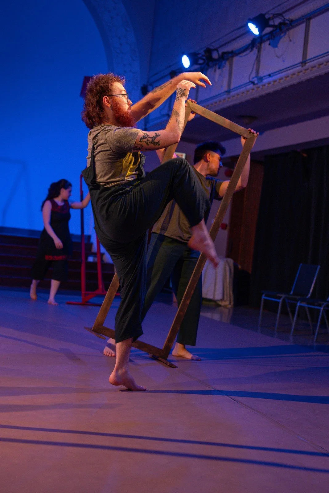 A performer balances against a wooden frame during a movement sequence.