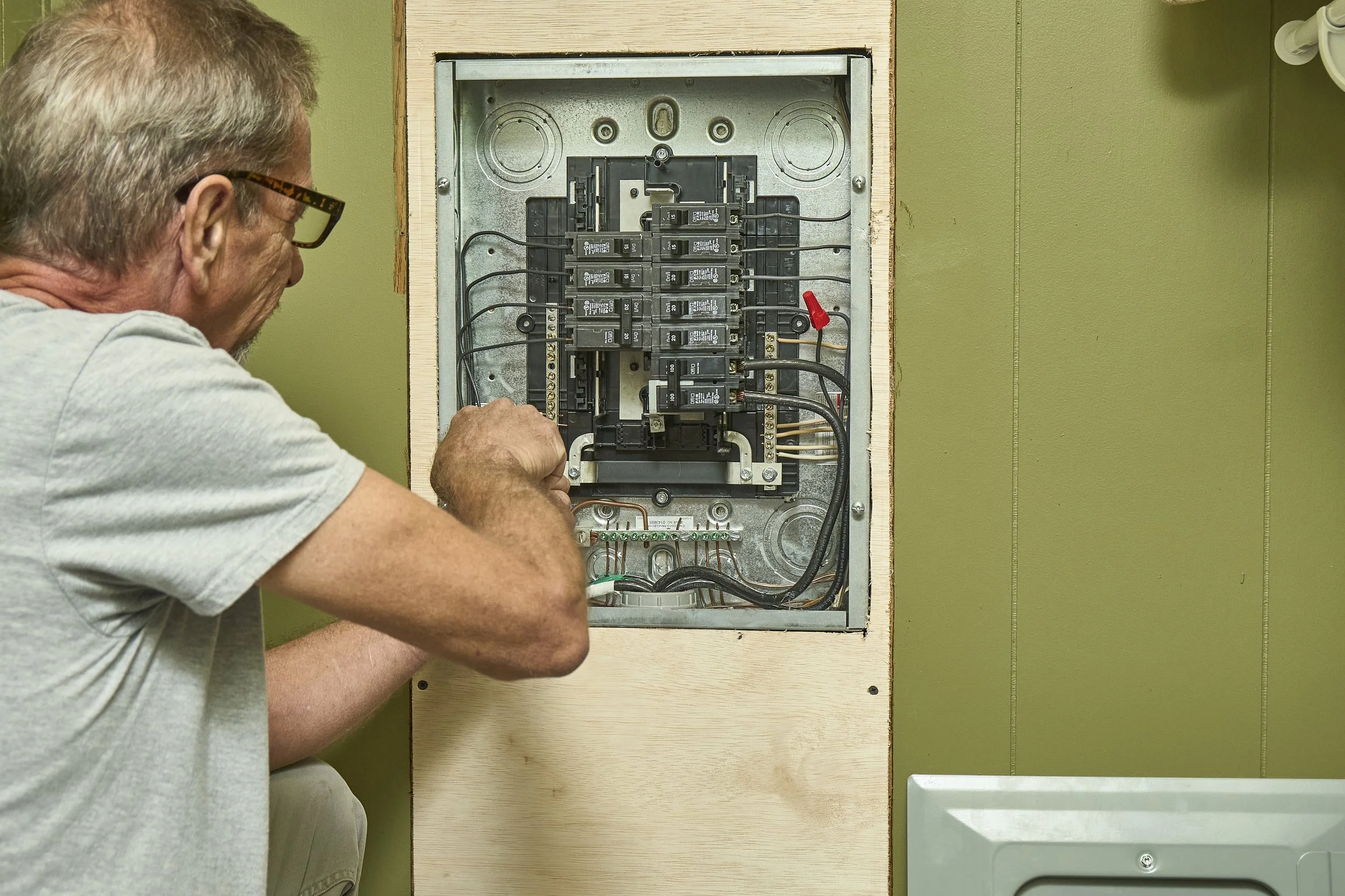 Kennedy Electric electrician checking breakers inside an open residential panel with the dead front removed.