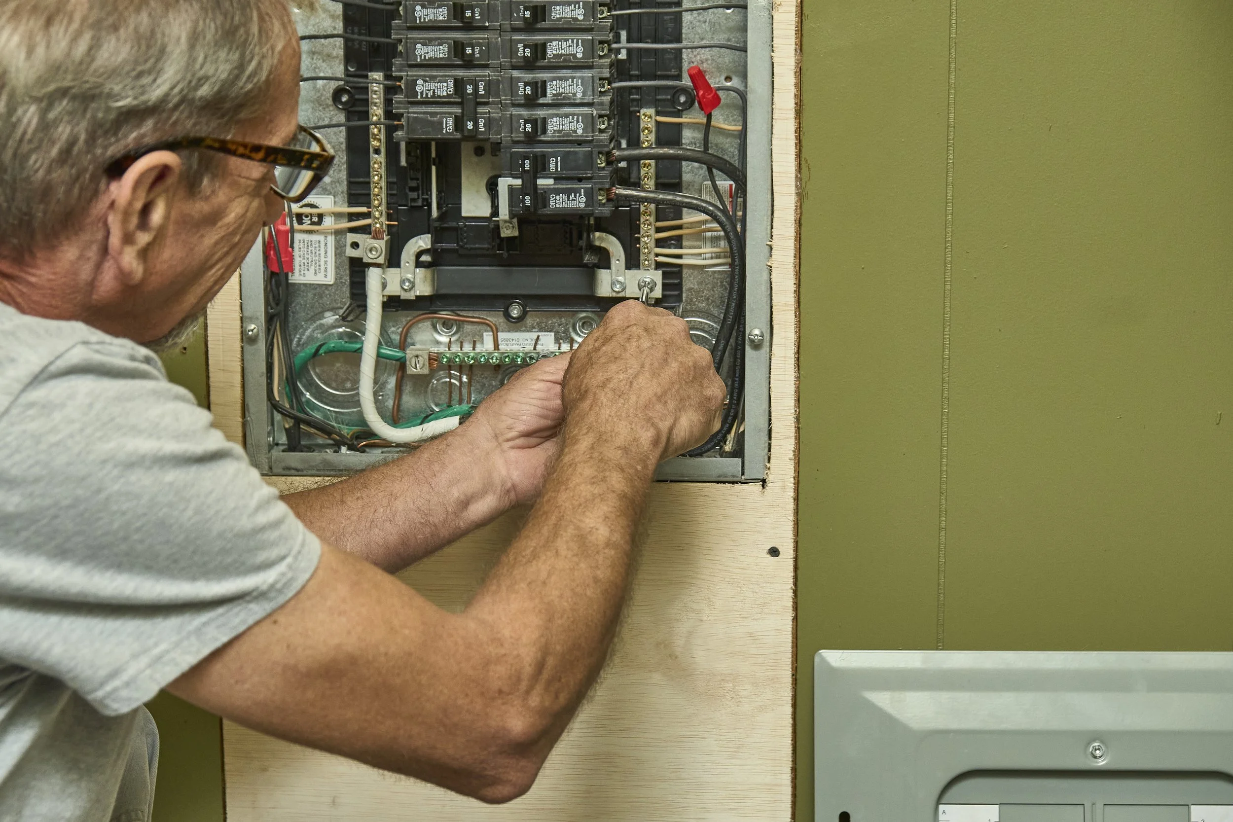 Electrician working inside an open breaker panel with a homeowner looking on.