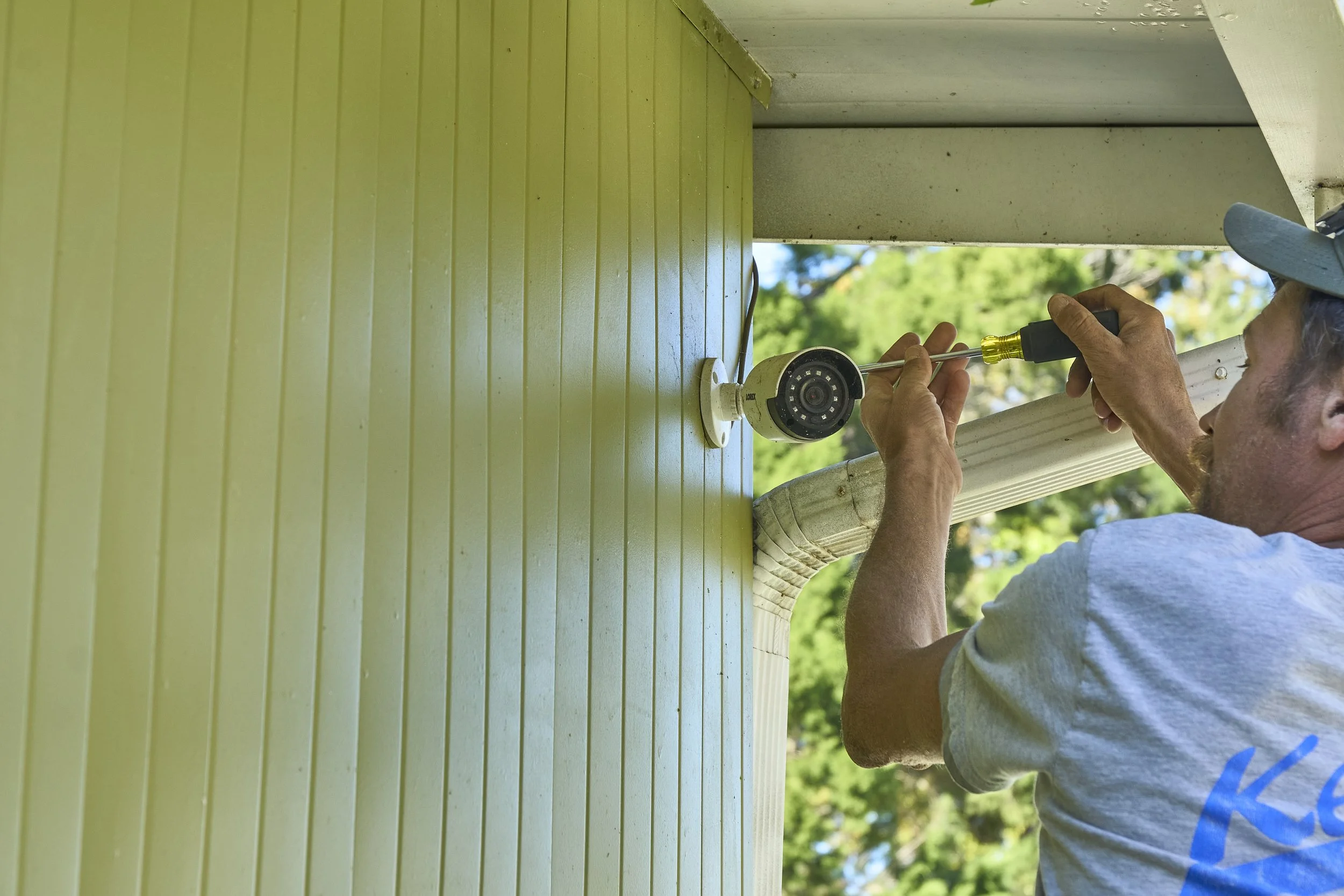 Electrician (Kennedy shirt) at an open exterior junction/disconnect box on green siding