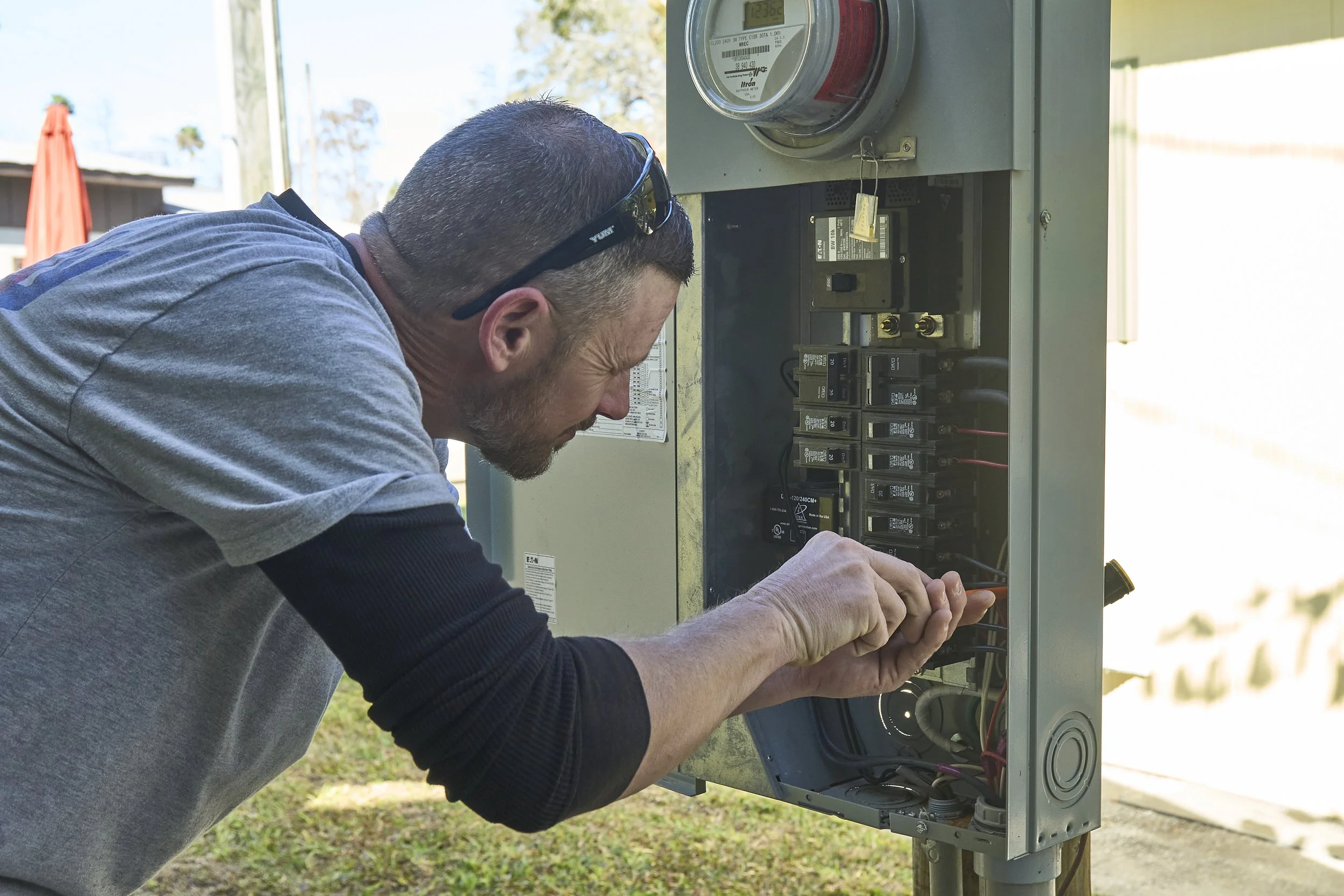 Man at an open exterior breaker panel/meter working