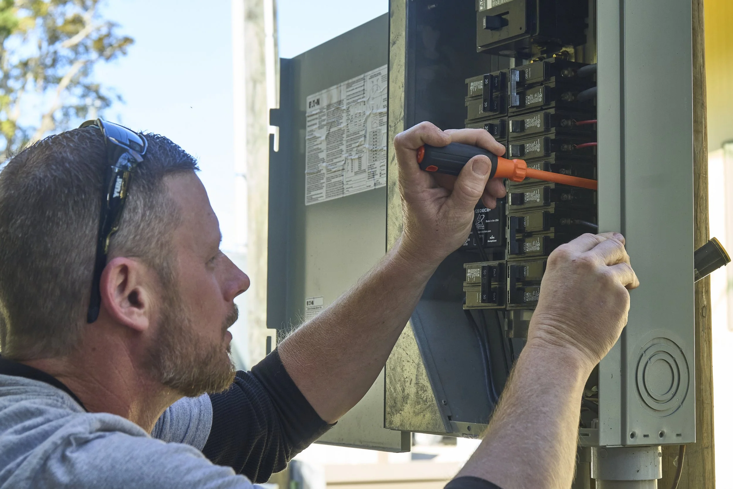 Man at an open exterior breaker panel with an orange screwdriver