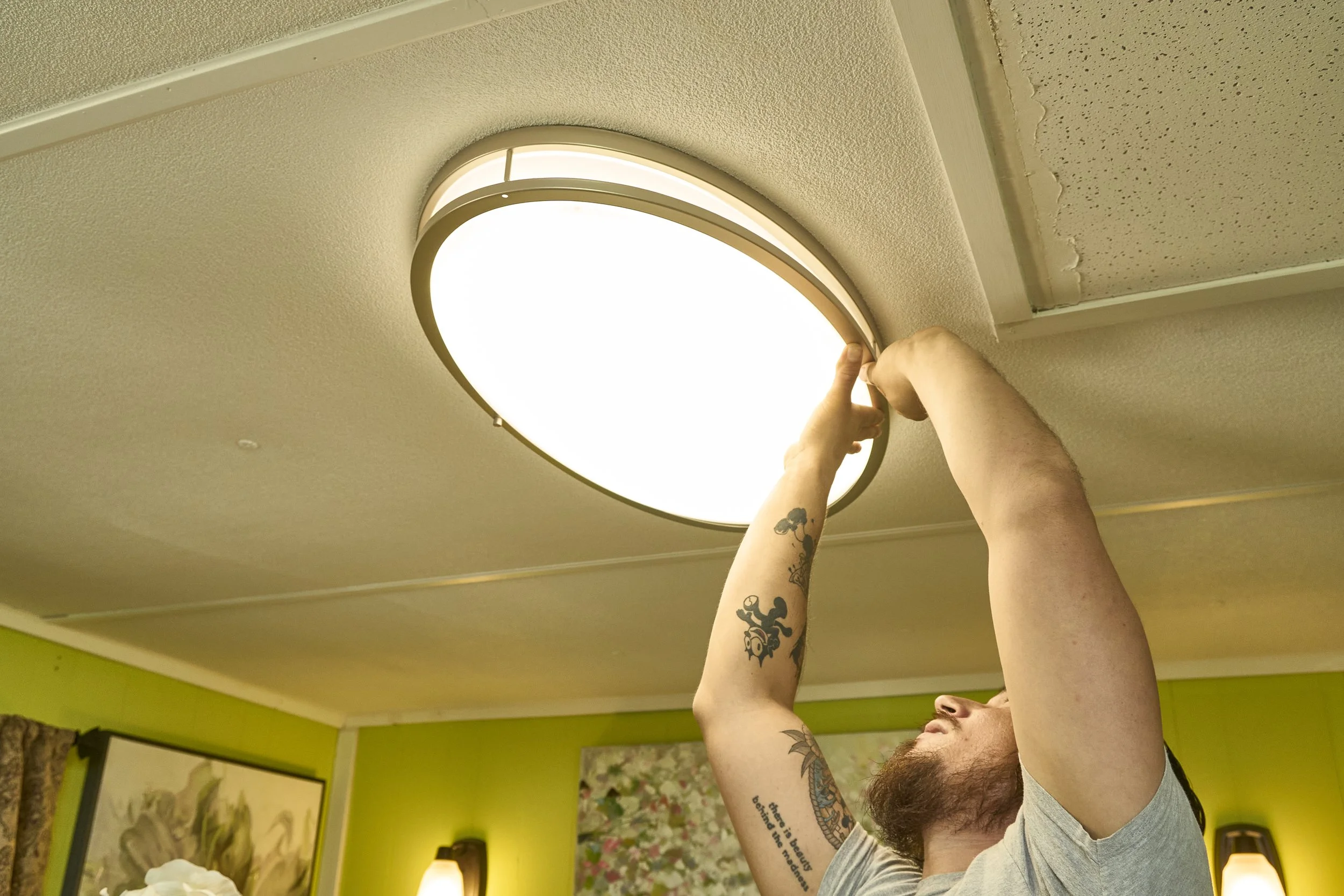 Man installing a round flush ceiling light fixture indoors