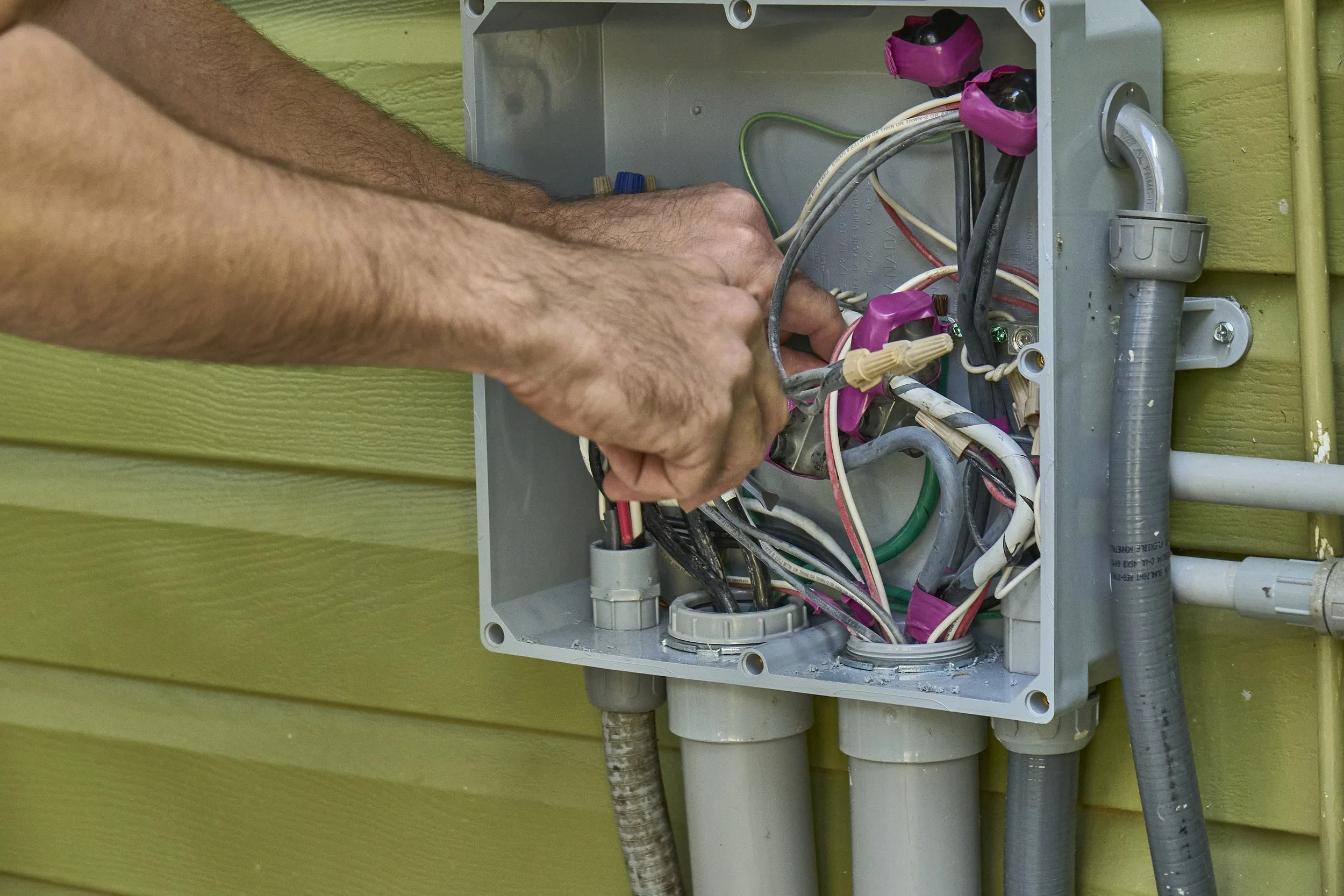 Person at an open exterior junction box with wires, green siding