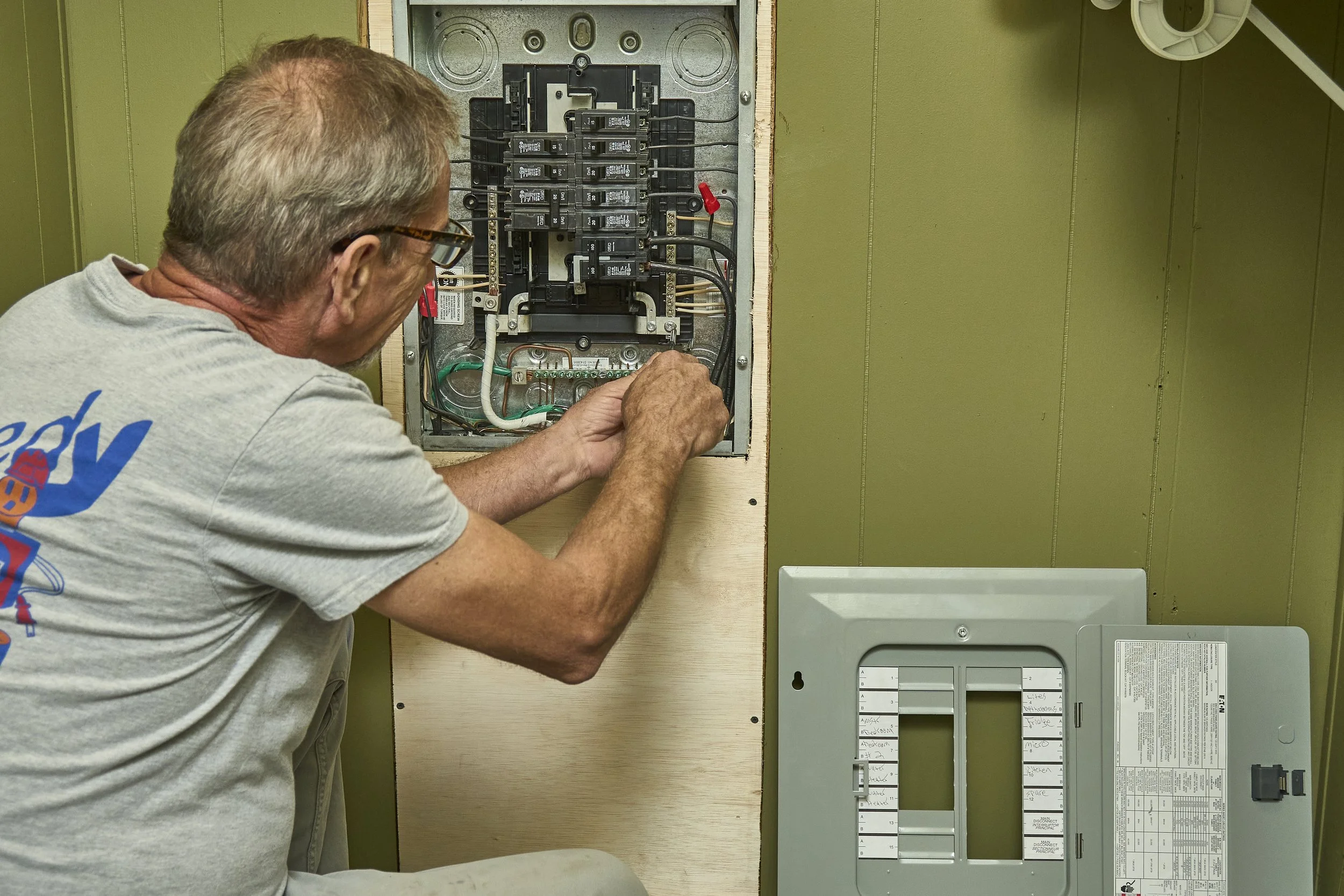 Electrician showing a homeowner a breaker inside an open home electrical panel.
