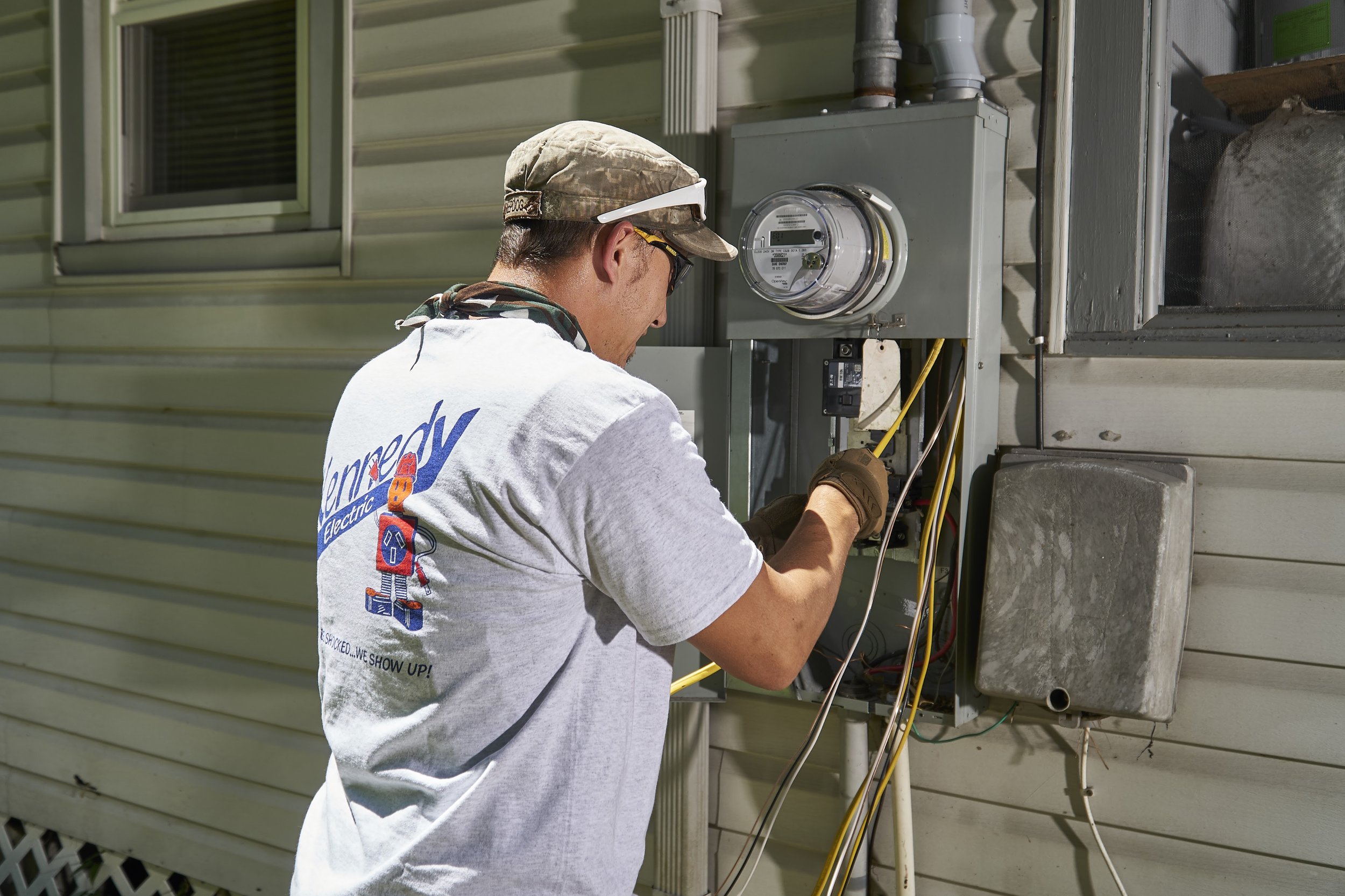 Electrician working at an exterior electric meter + disconnect on the side of a house