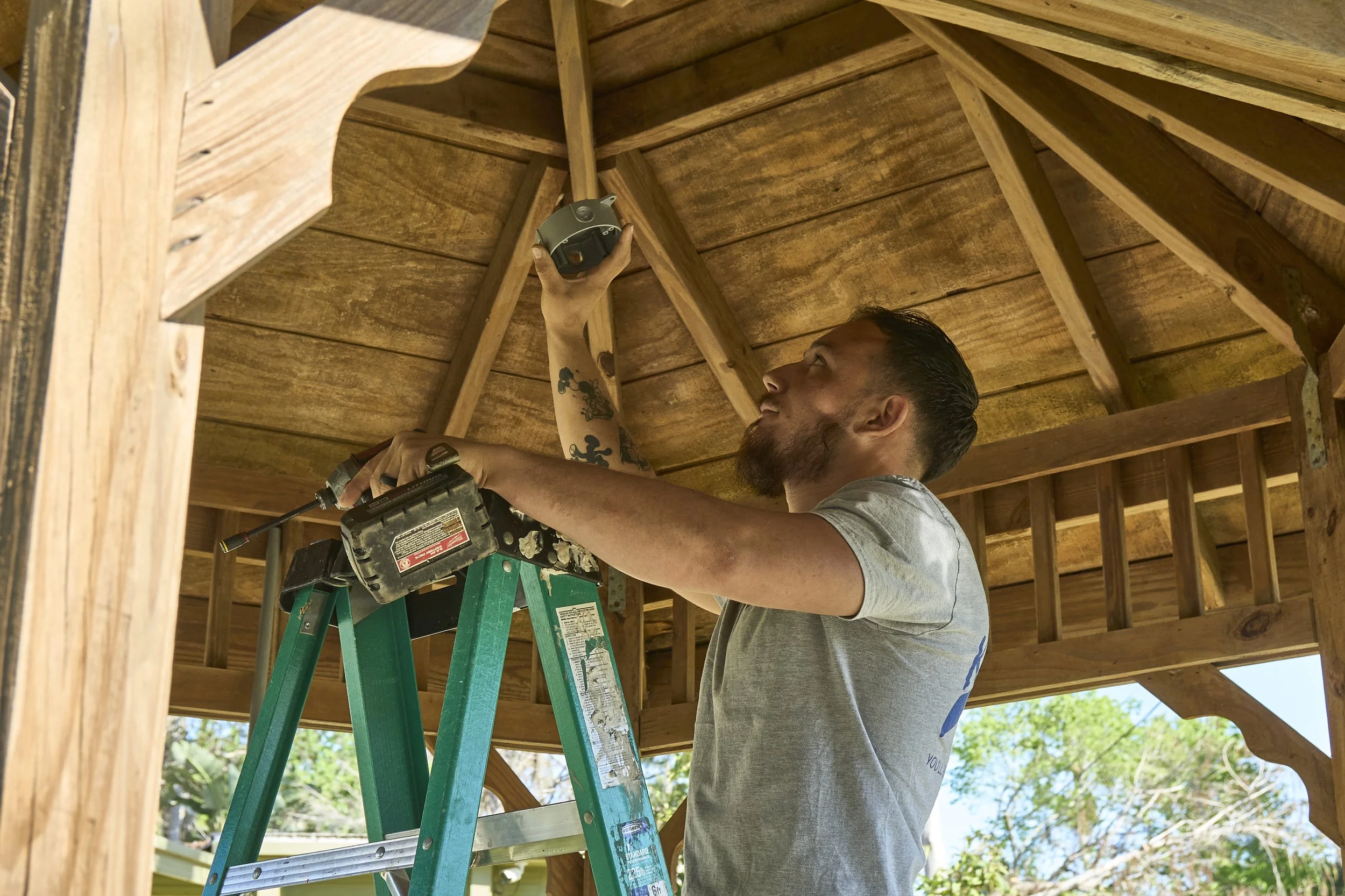 Man on a ladder working under a wood gazebo ceiling