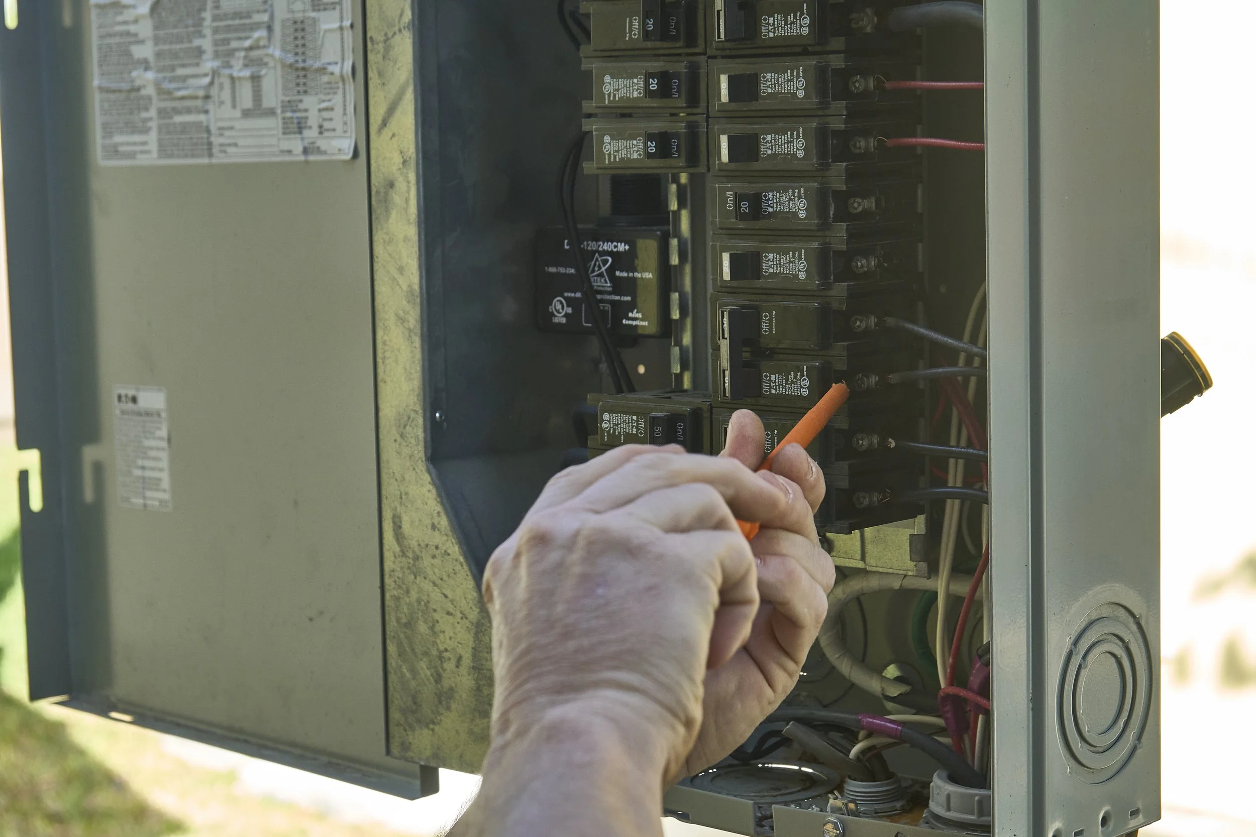 Hands with an orange screwdriver at an open exterior breaker/meter panel