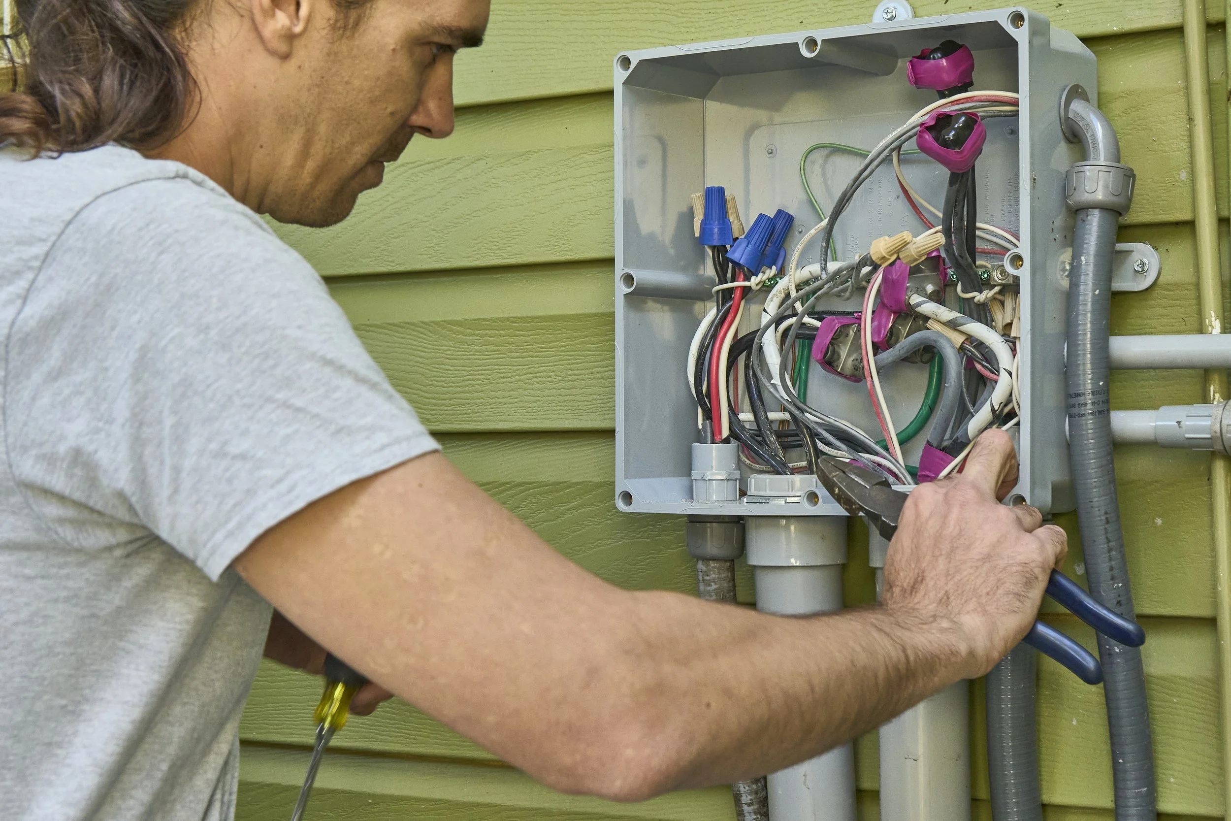 Person at an open exterior junction box with wires on green siding
