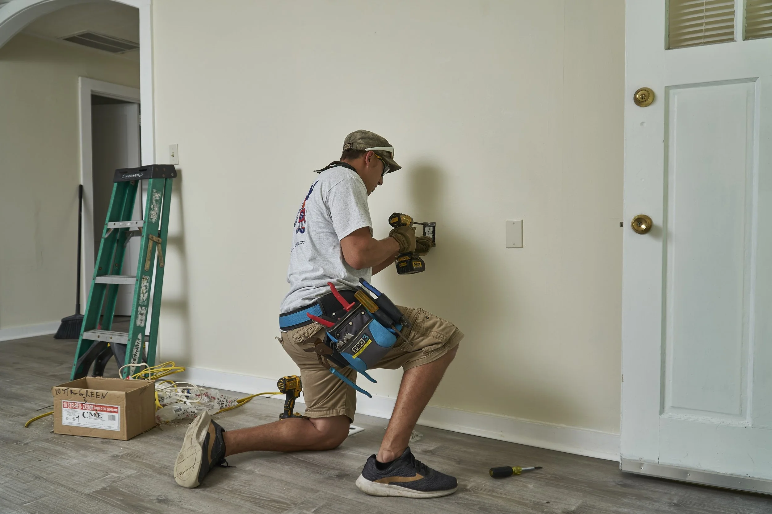 Electrician kneeling working on an interior wall box, ladder nearby