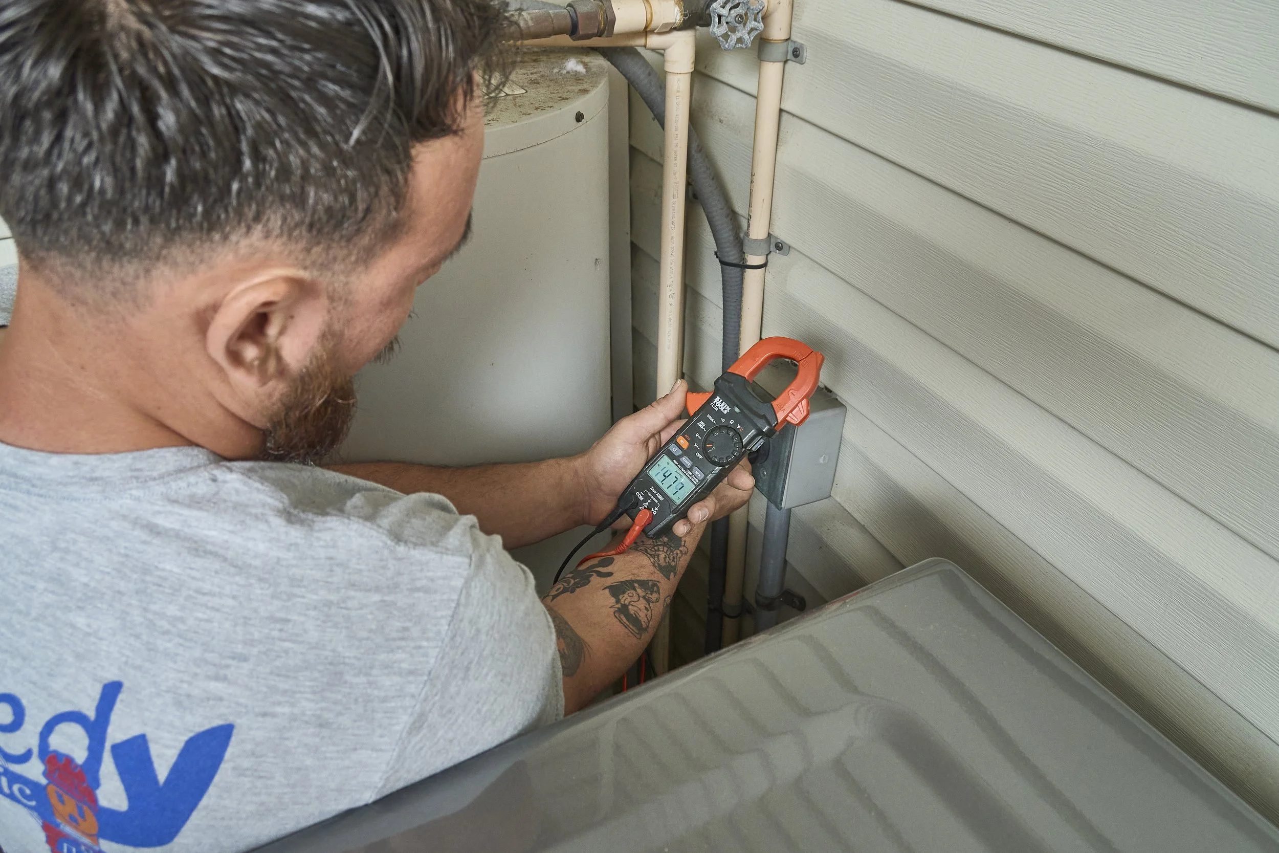 Electrician testing wiring with a clamp meter in a wall cavity