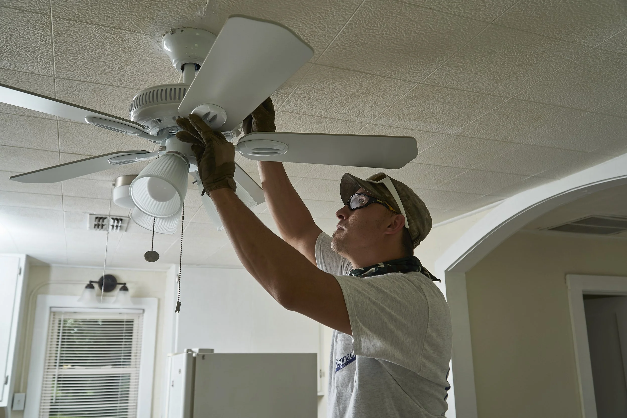 Electrician installing a white ceiling fan indoors