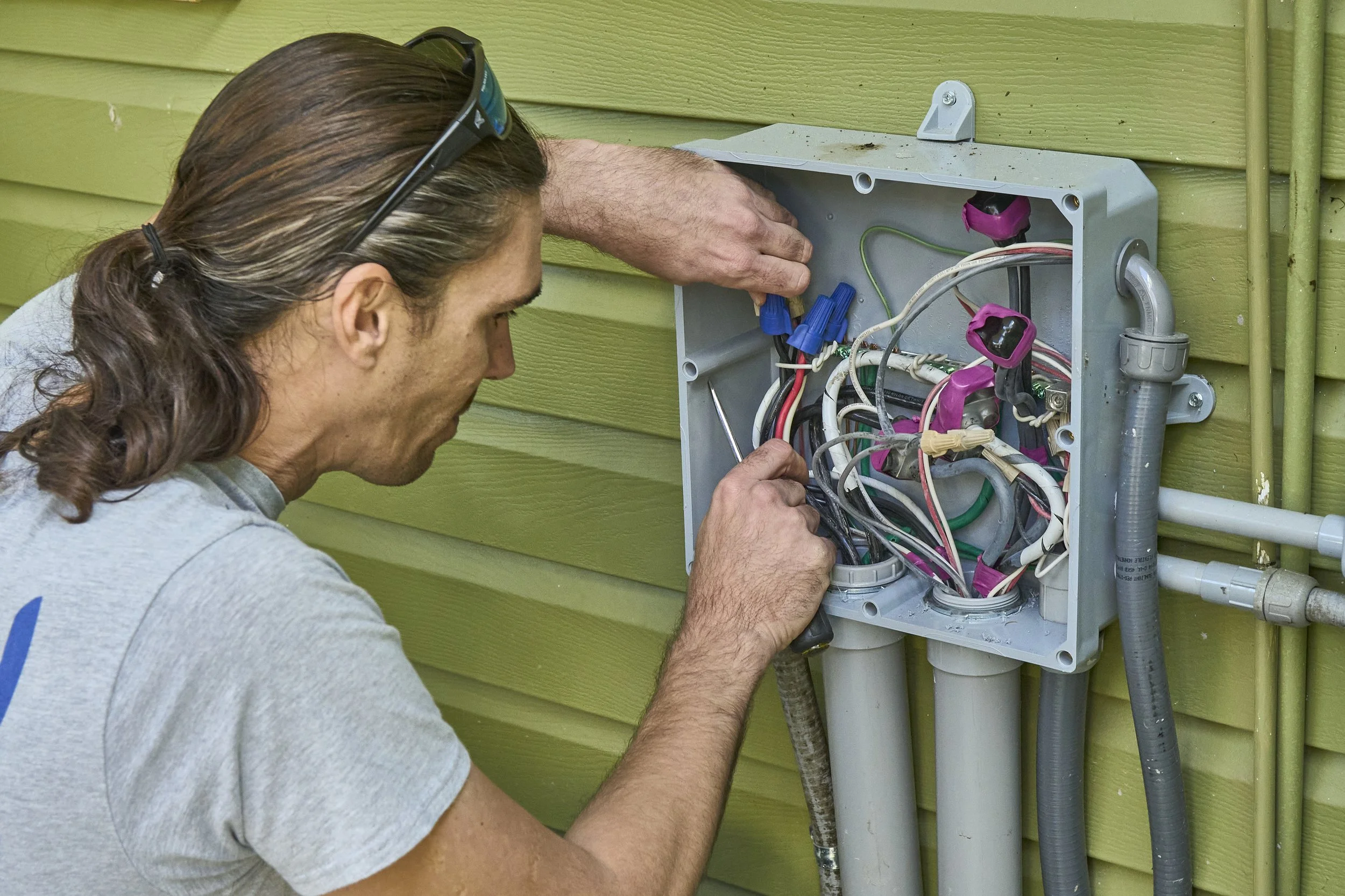 Electrician at an open exterior junction box with wires on green siding