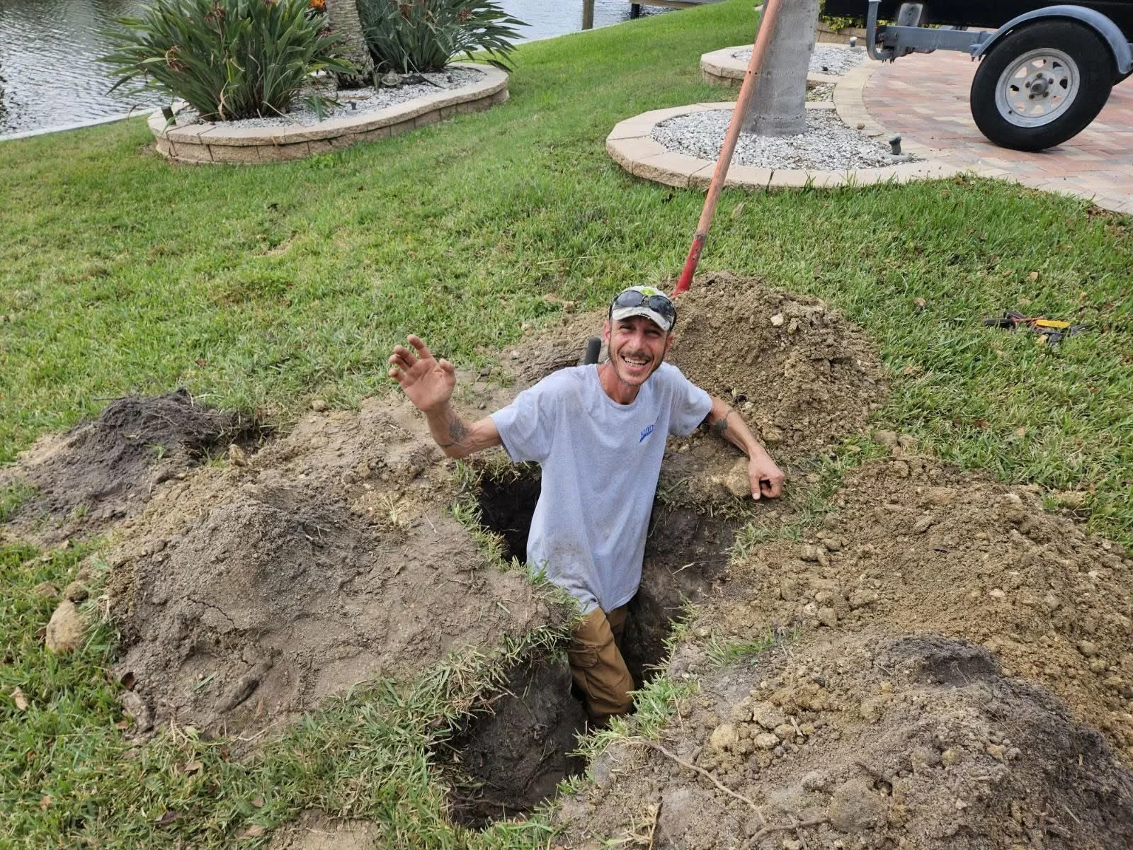 Worker standing in a dug hole/trench in a yard with a shovel