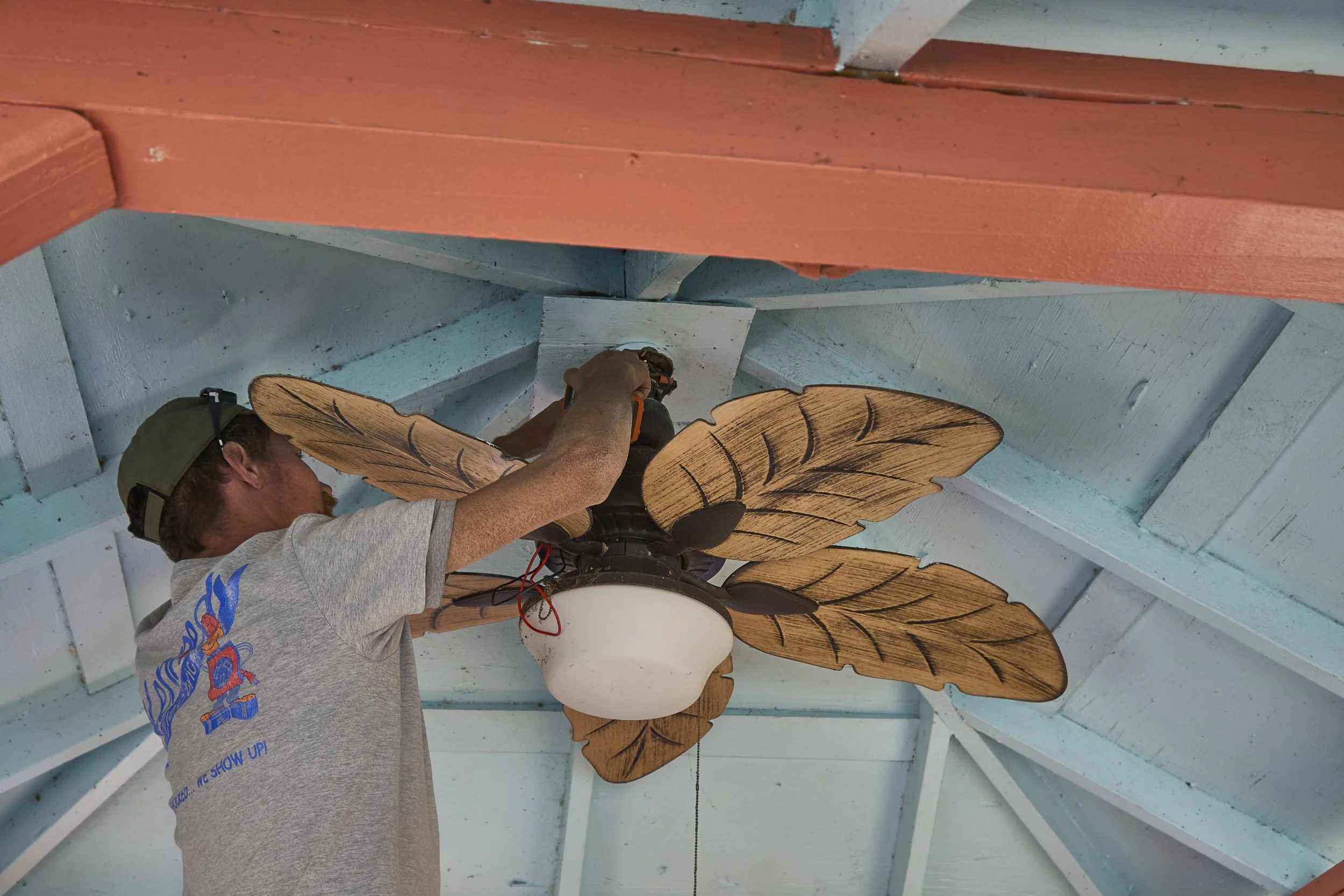 Electrician installing a palm-leaf ceiling fan with light under a porch