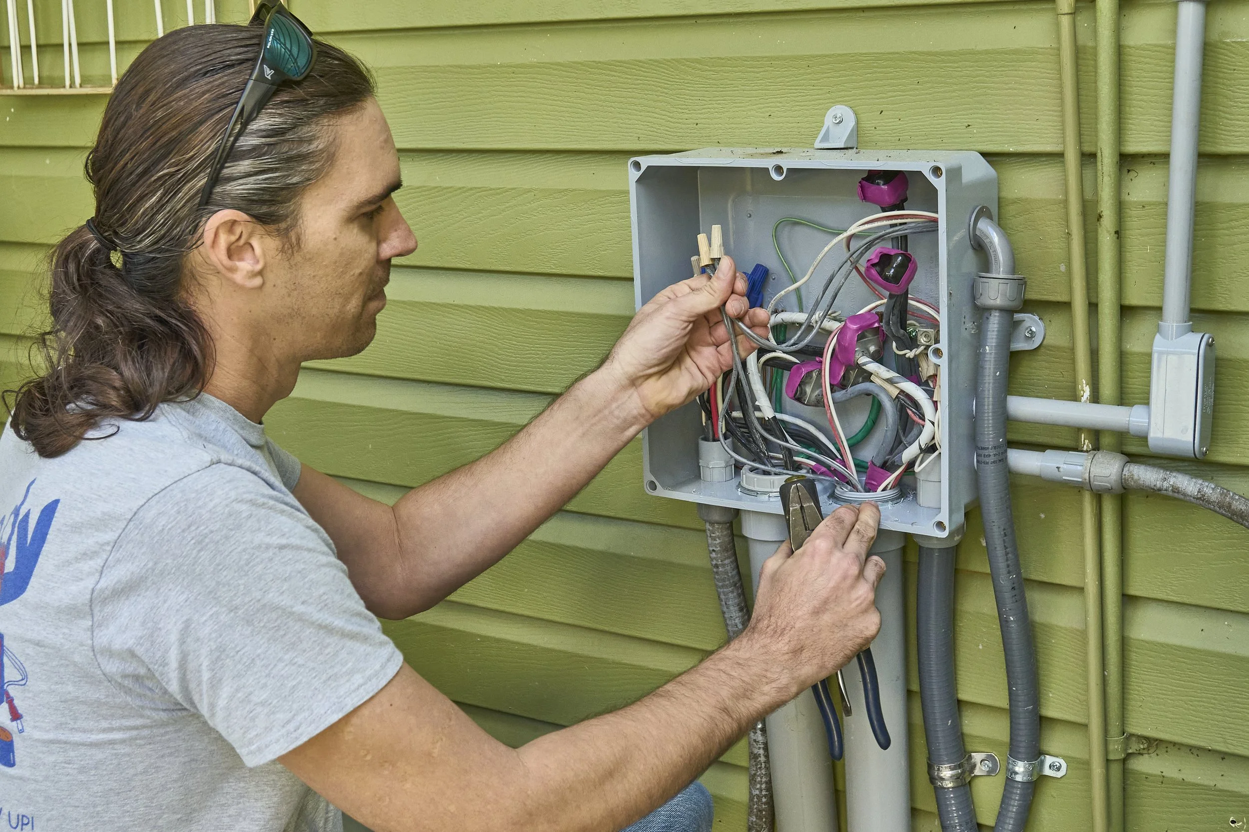 Electrician (Kennedy shirt) at an open exterior junction/disconnect box with wires