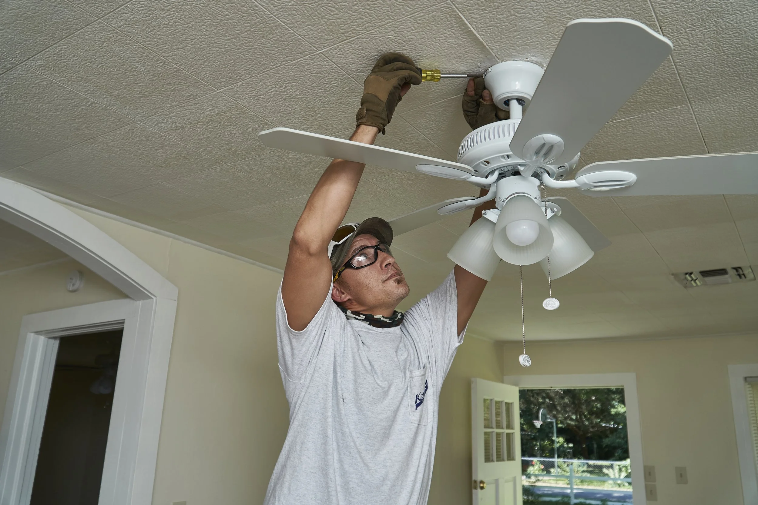 Electrician installing a ceiling fan with light indoors