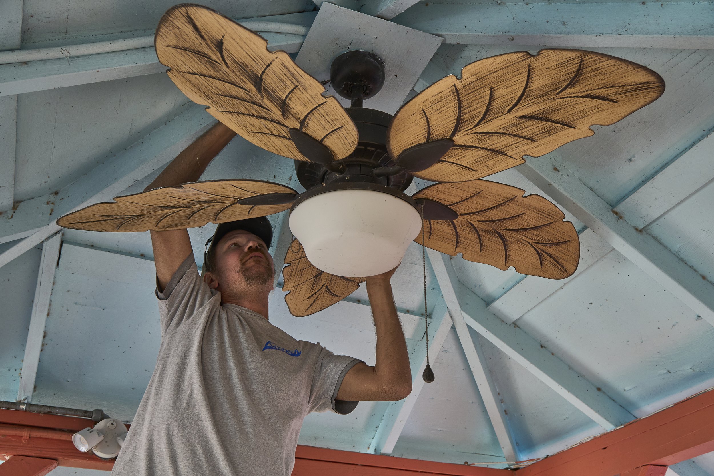 Electrician installing a palm-leaf ceiling fan under a porch/gazebo